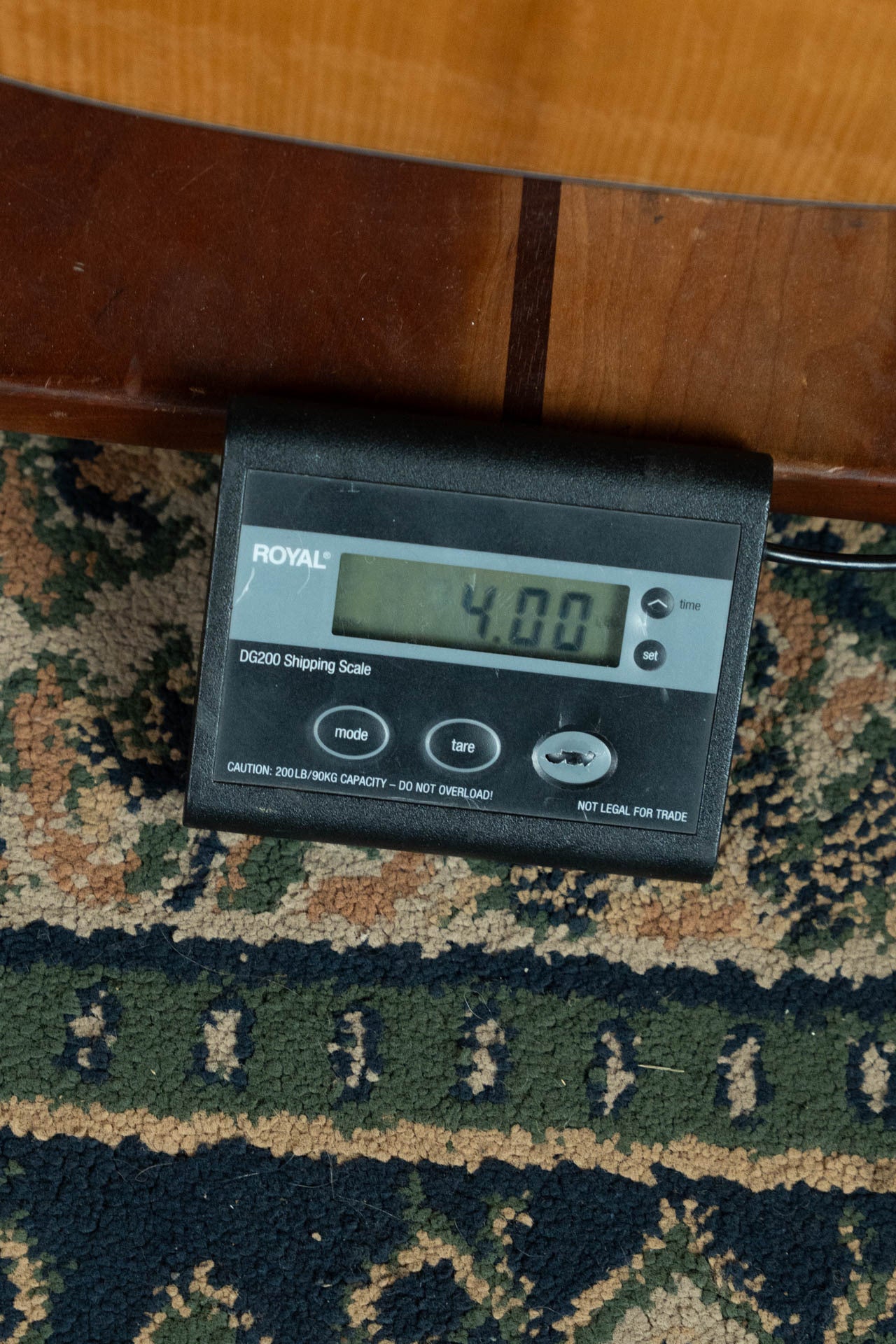 A digital shipping scale on patterned carpet reads 4.00 pounds, ideal for weighing your Boucher Guitars BG-42T-G Bluegrass Goose Series Adirondack/Mahogany Dreadnought Gold Pack Acoustic Guitar #1035.