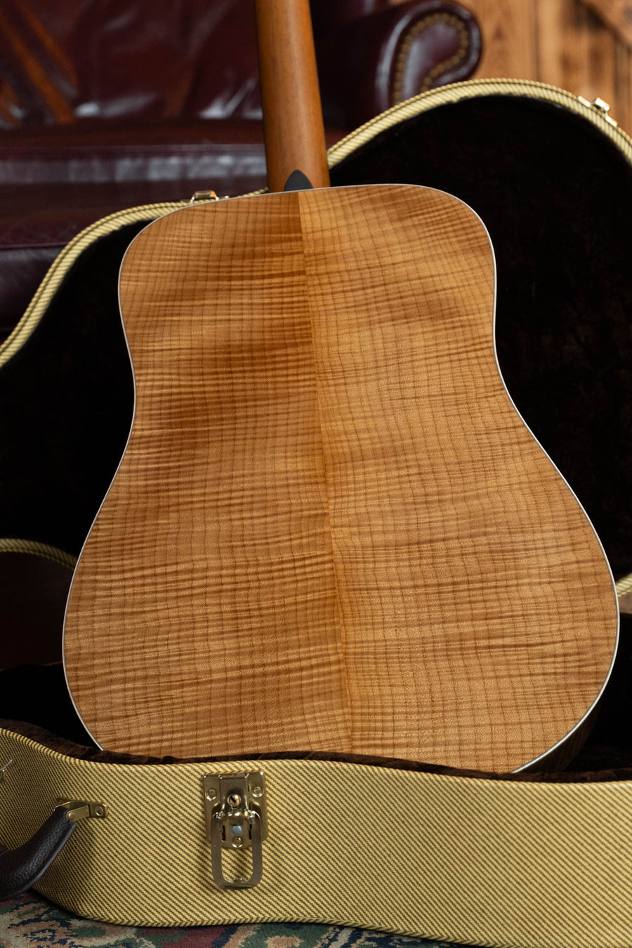 The back of the Boucher Guitars GR-SG-162T Grande Reserve Dreadnought (#1037), featuring a flamed maple finish, is displayed in an open, dark-lined hard-shell case secured with a gold latch.