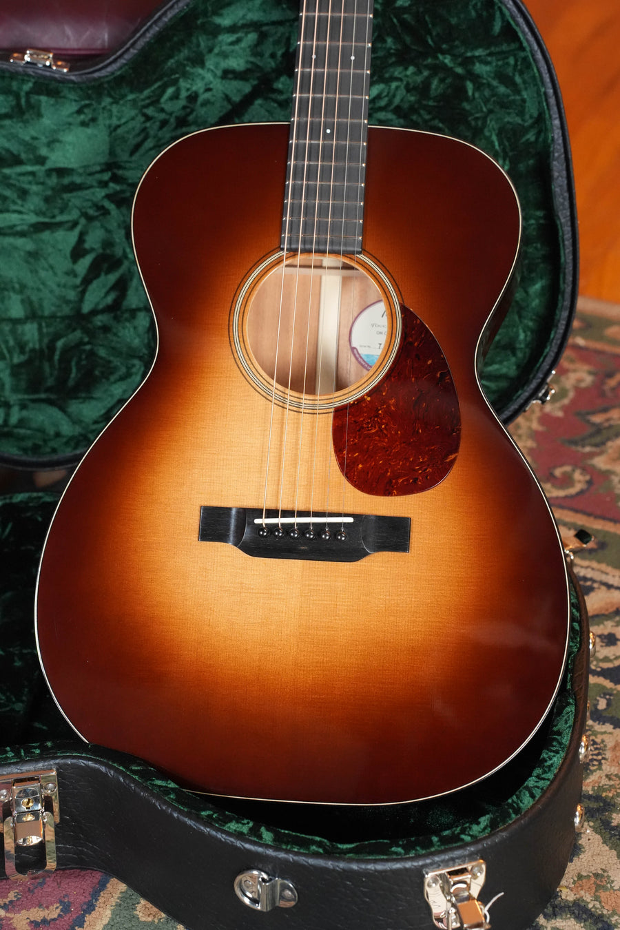 A Bourgeois Country Boy Touchstone Series Sitka/Mahogany Sunburst Orchestra Model Acoustic Guitar #0252 rests in an open green velvet-lined case. The tortoiseshell pickguard and visible neck are displayed on a patterned rug.