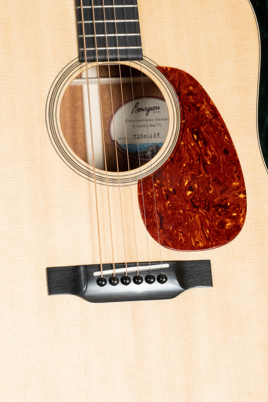 Close-up of a Bourgeois Country Boy Touchstone Series Sitka/Mahogany Natural Dreadnought Acoustic Guitar #1239 body, showing the Sitka spruce top, soundhole with partial label, fretboard, tortoiseshell-style pickguard, bridge, and strings.