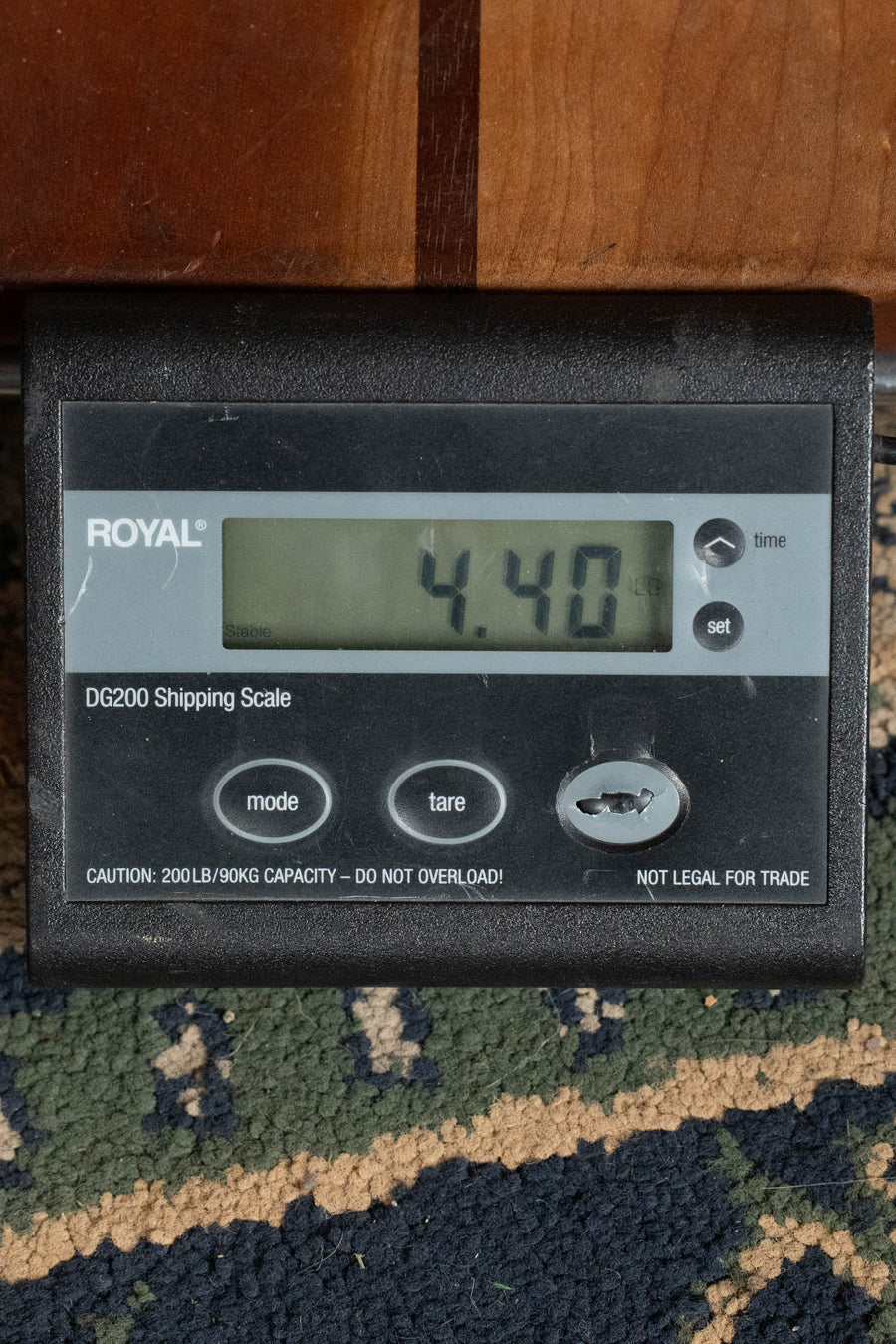 A digital shipping scale reads 4.40 pounds as the black ROYAL DG200 sits on a patterned carpet near wooden furniture, suggesting the presence of a Bourgeois Country Boy Touchstone Series Sitka/Mahogany Natural Dreadnought Acoustic Guitar #1239.