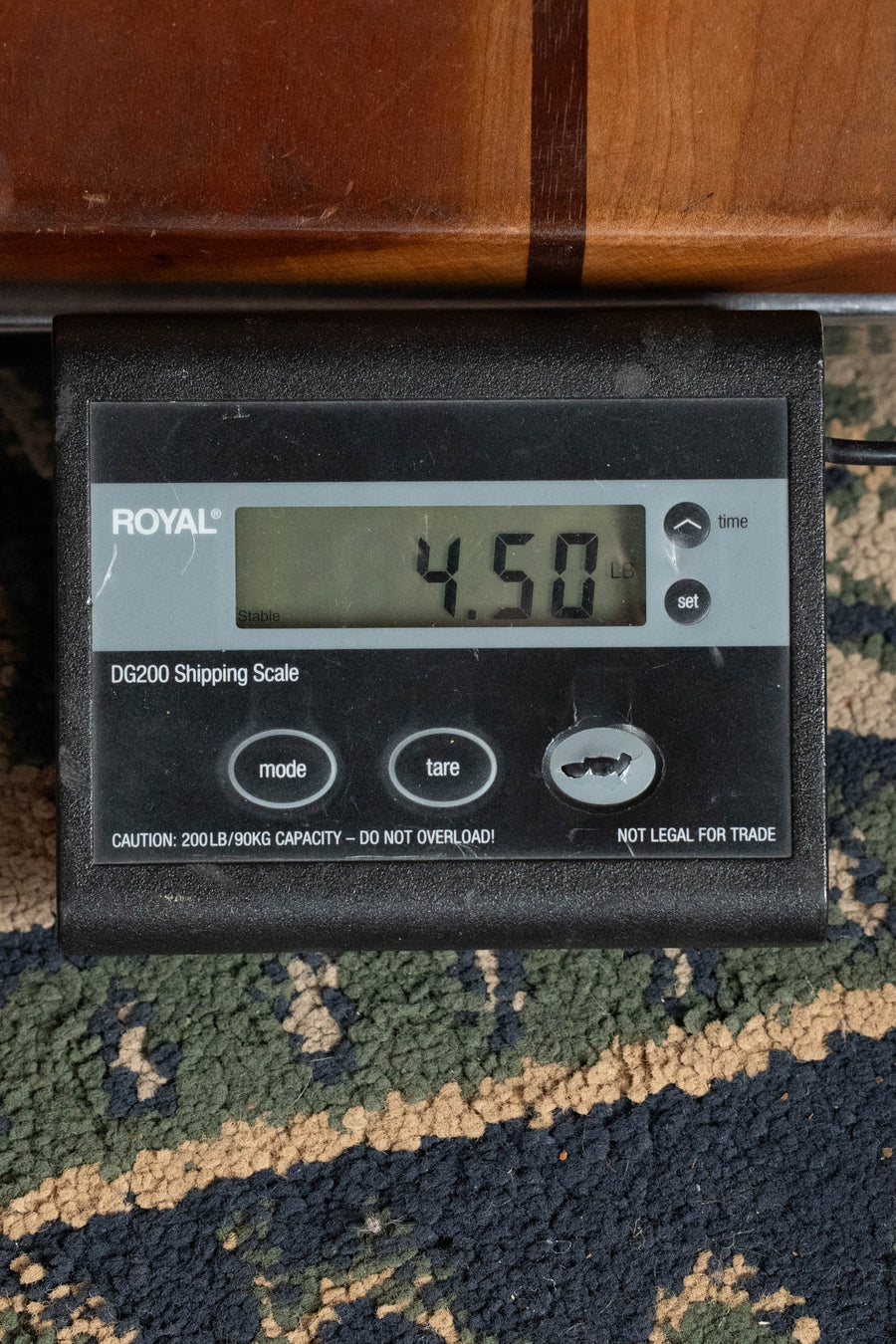 A digital shipping scale shows 4.50 lbs as it weighs a Bourgeois D Vintage/TS Touchstone Series Sitka/Rosewood Dreadnought Acoustic Guitar #9282, sitting on patterned carpet near wood, with the black scale’s labeled buttons in view.