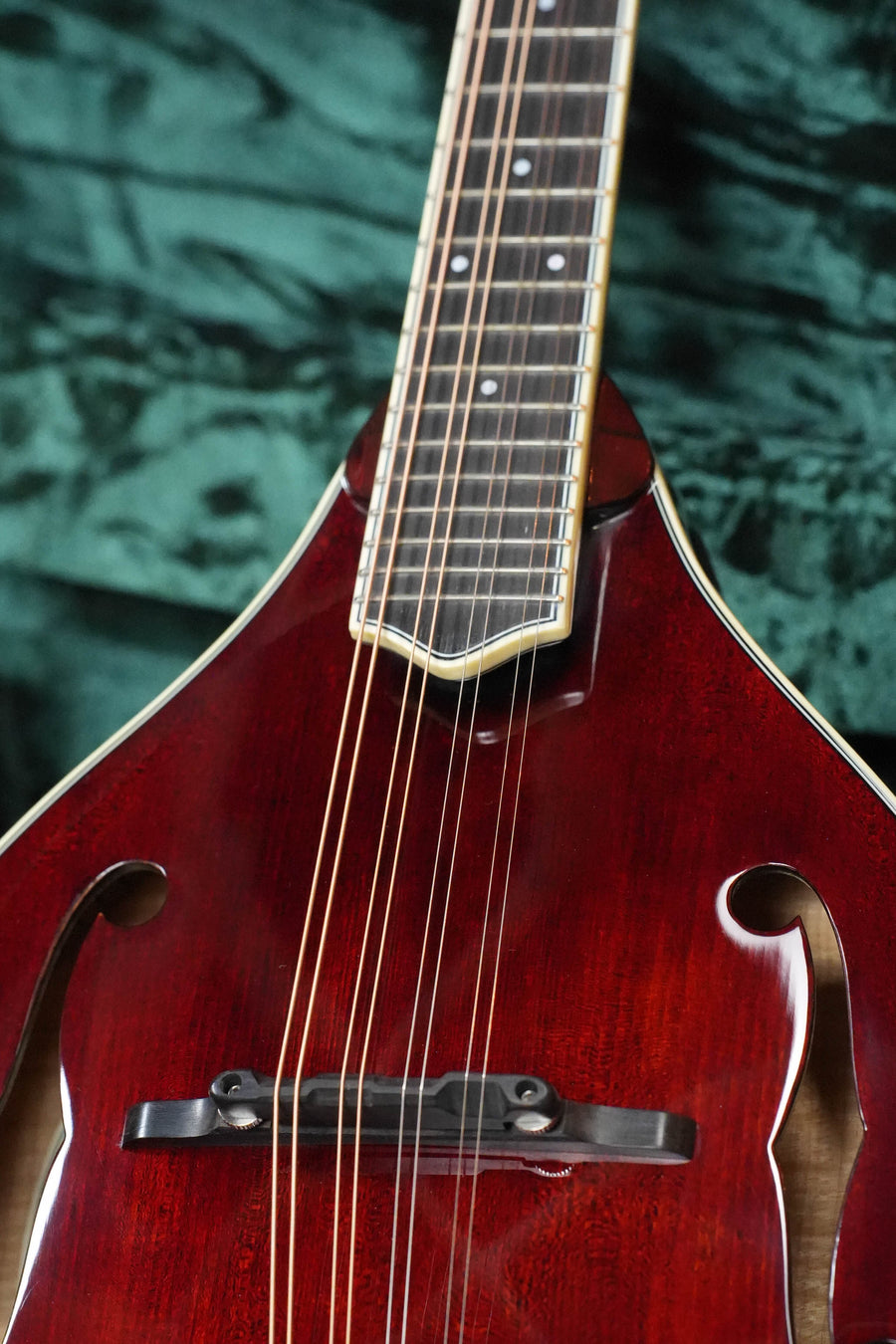 Close-up of a Bourgeois TAS Exclusive M5-A-CR Aged-Tone Adirondack/Maple Cordovan Red A-Style Mandolin #2119, featuring its strings, bridge, and neck against a dark green textured background—a premium professional model.