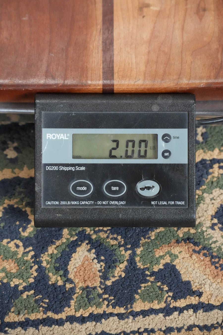 A black digital shipping scale shows a weight of 2.00 lbs on patterned carpet, with part of a Bourgeois TAS Exclusive M5-A-CR Aged-Tone Adirondack/Maple Cordovan Red A-Style Mandolin #2119 visible above it.