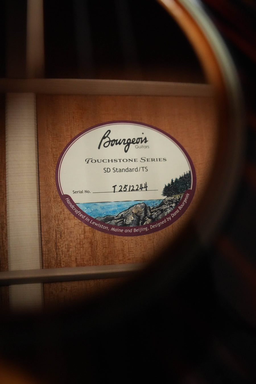 Close-up through the sound hole of a Bourgeois The Standard SDS/TS Touchstone Series Slope Shoulder Sunburst Dreadnought #2244, showing the label with model details and scenic artwork inside.