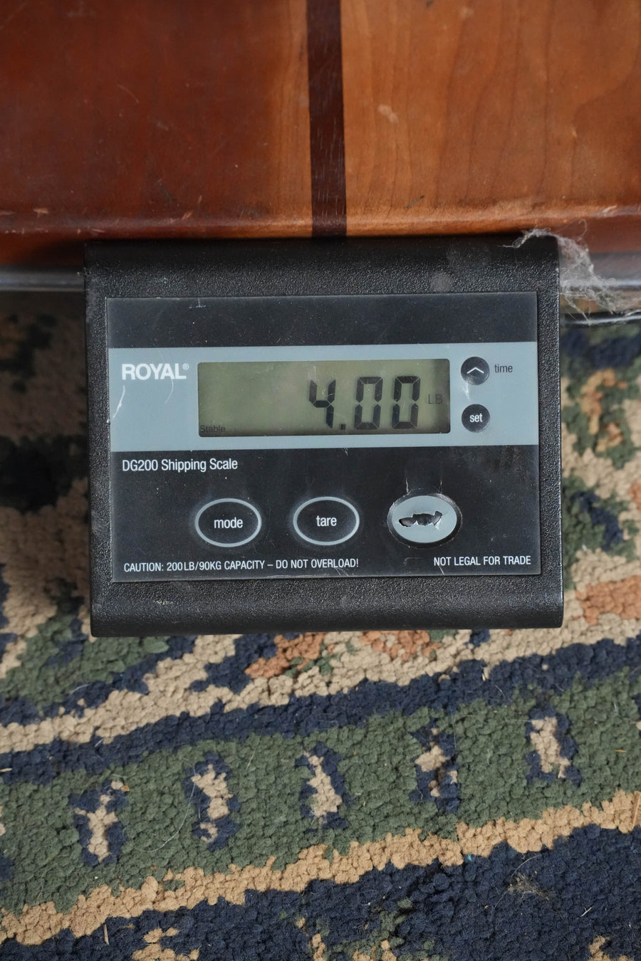 A digital shipping scale on a patterned carpet shows 4.00 pounds—ideal for shipping the Bourgeois The Standard SDS/TS Touchstone Series Torrefied Sitka/Mahogany Slope Shoulder Sunburst Dreadnought Acoustic Guitar #2244. The Royal scale offers mode and tare buttons and capacity caution.