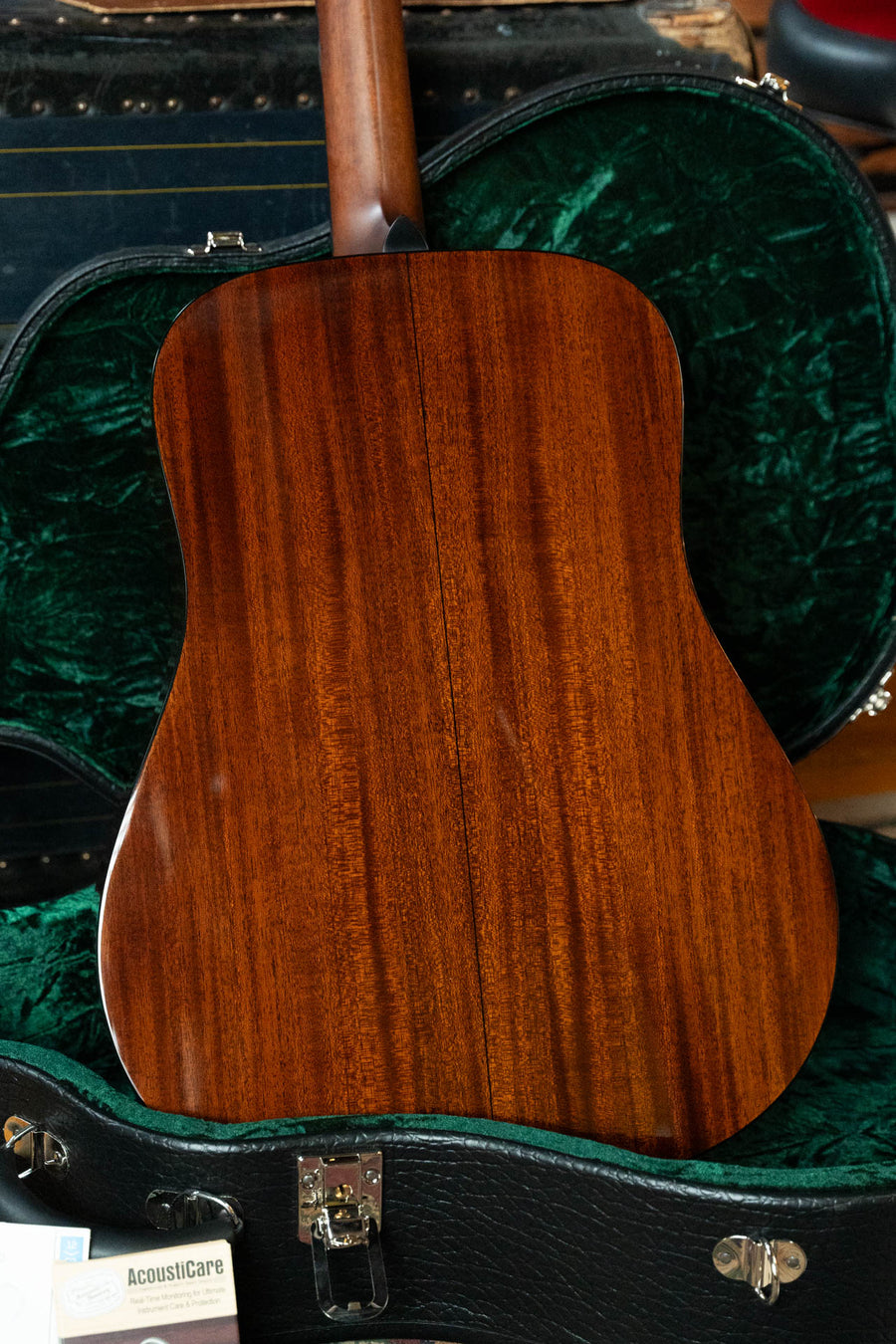 A close-up of the back of the Bourgeois Touchstone Country Boy Sitka/Mahogany Natural Dreadnought Acoustic Guitar #8237, resting in a partially open green velvet-lined case, reveals its glossy wood finish and neck.