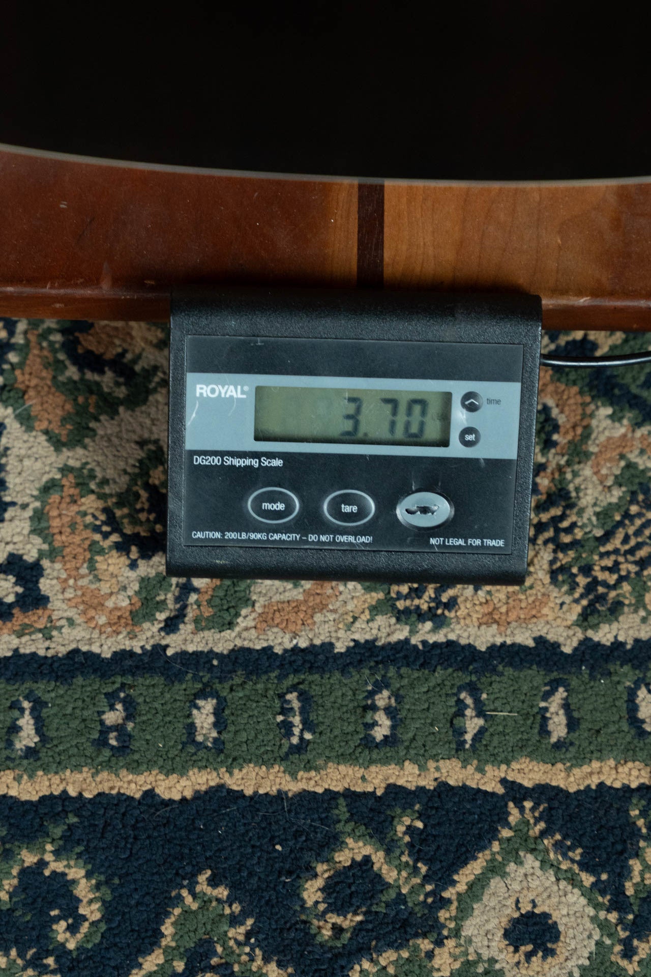 A digital shipping scale on a patterned carpet shows 37.01 pounds, likely the exact weight of a Bourgeois Blues PSBB-LDBO-S Satin Professional Series All Mahogany OO Acoustic Guitar #1197, ready to be shipped.