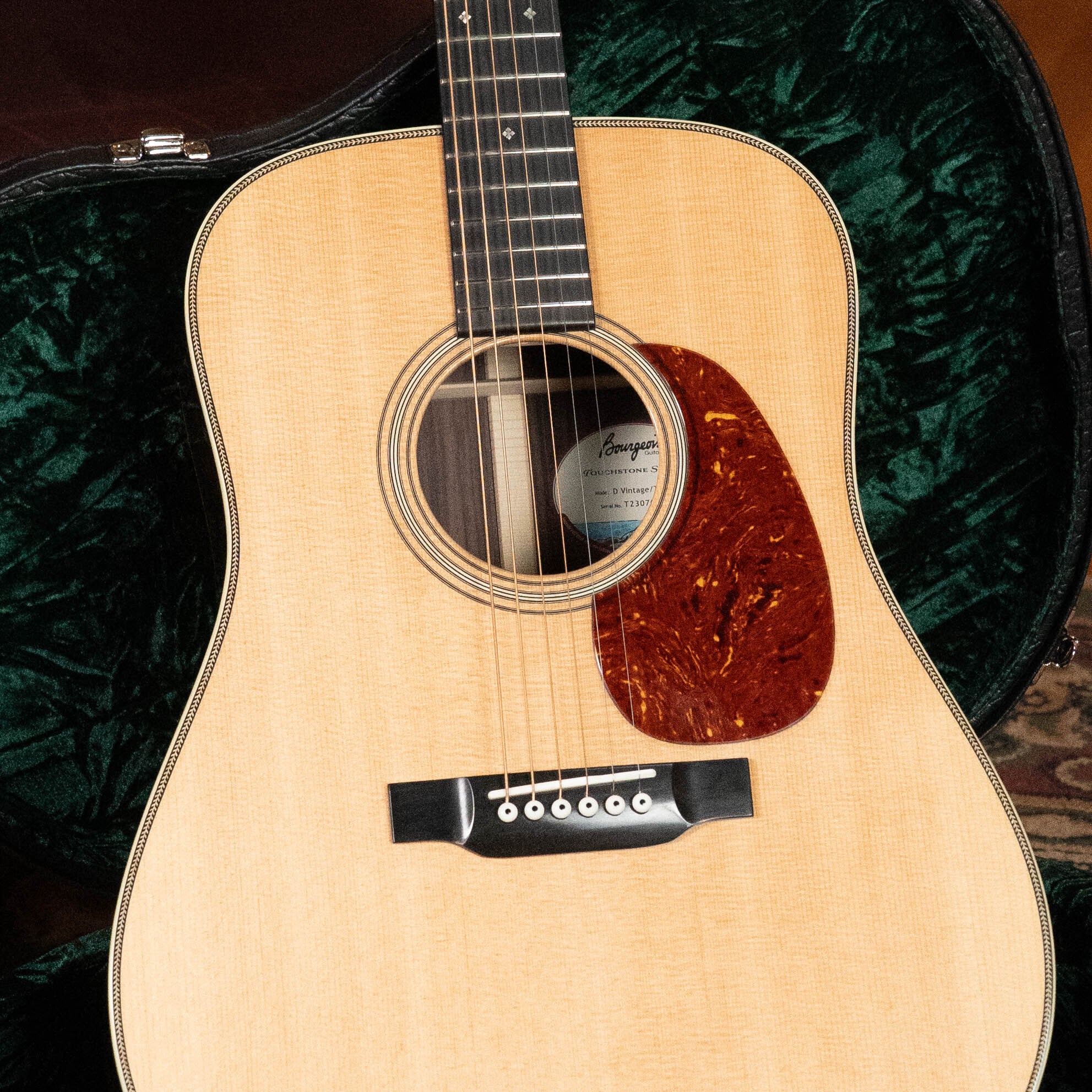 A close-up of a Bourgeois D Vintage/TS Touchstone Series Dreadnought Acoustic Guitar #7014 with six strings, an old-growth Alaskan Sitka spruce top, tortoiseshell pickguard, and an open green velvet-lined case in the background.
