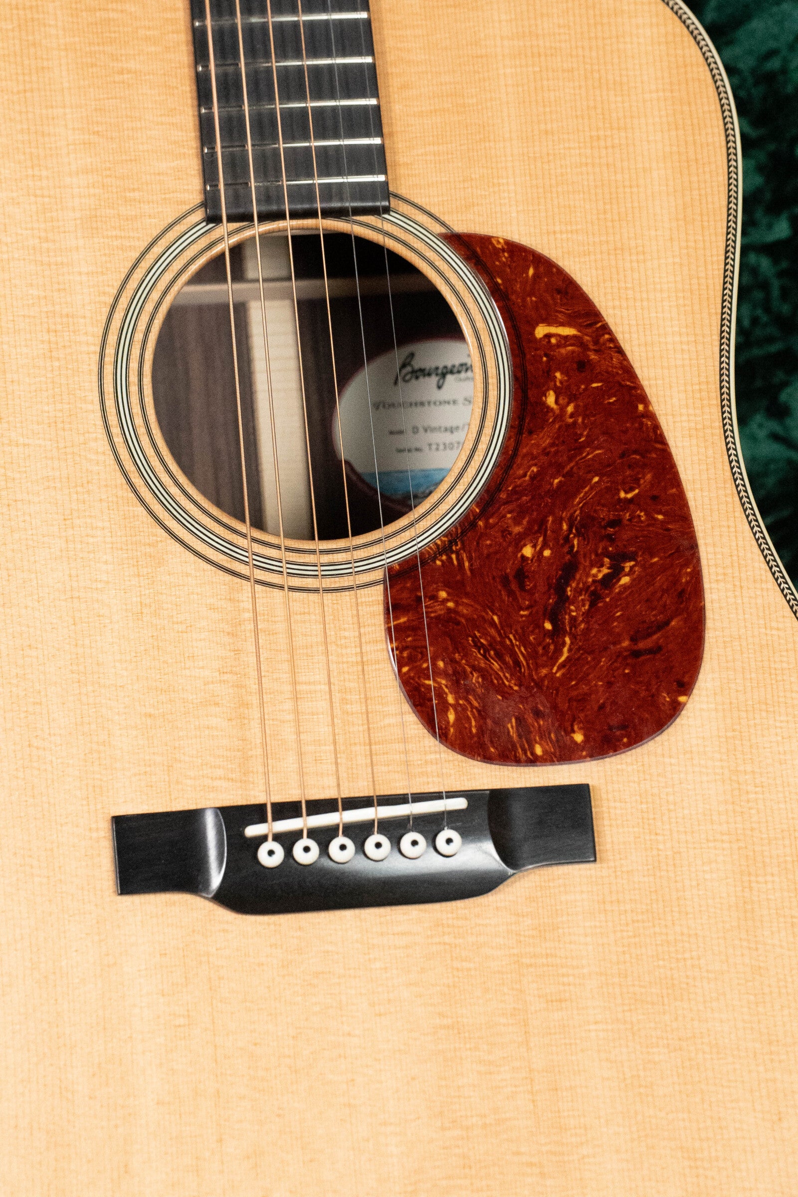 Close-up of the Bourgeois D Vintage/TS Touchstone Series Dreadnought Acoustic Guitar #7014 shows its sound hole, tortoiseshell-pattern pickguard, strings, six-pin bridge, and label noting Old-Growth Alaskan Sitka Spruce construction.