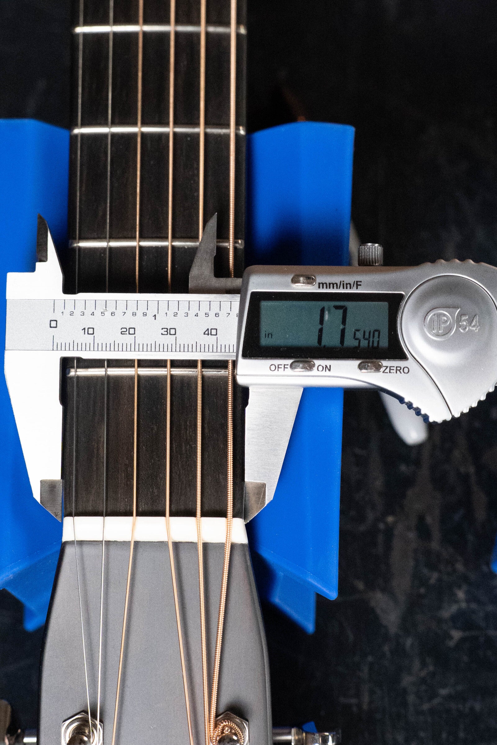 A digital caliper shows the neck width at the nut of a Bourgeois D Vintage/TS Touchstone Series Dreadnought Acoustic Guitar #7014 as 47.54 mm, with the guitar held in blue supports and the caliper positioned above the strings.