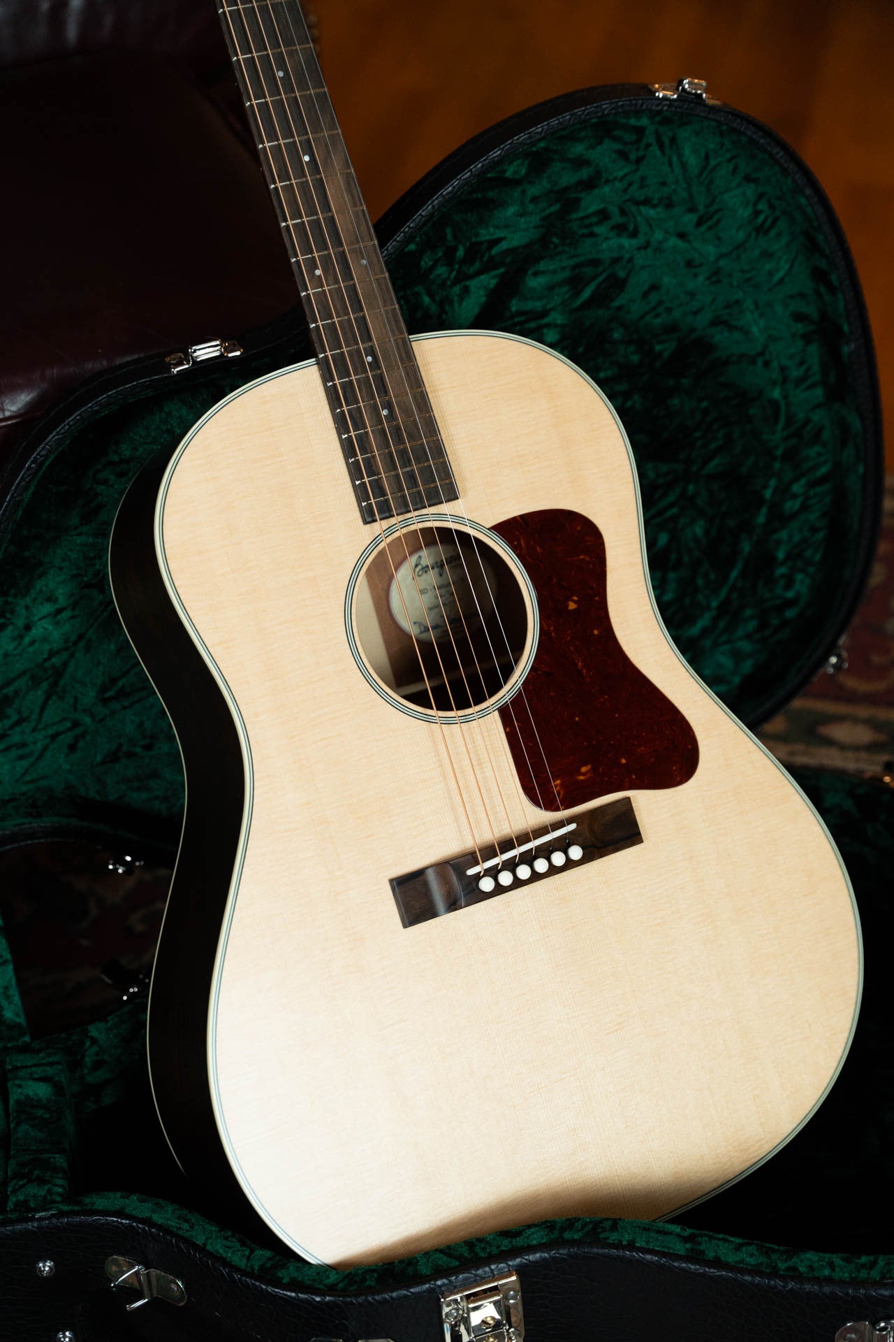 The Boucher Guitars Bourgeois PSN-SD-S Satin Professional Series The Natural Sitka/Mahogany Slope Shoulder Dreadnought Acoustic Guitar #1174, with a tortoiseshell pickguard, sits upright in an open, dark green velvet-lined case.
