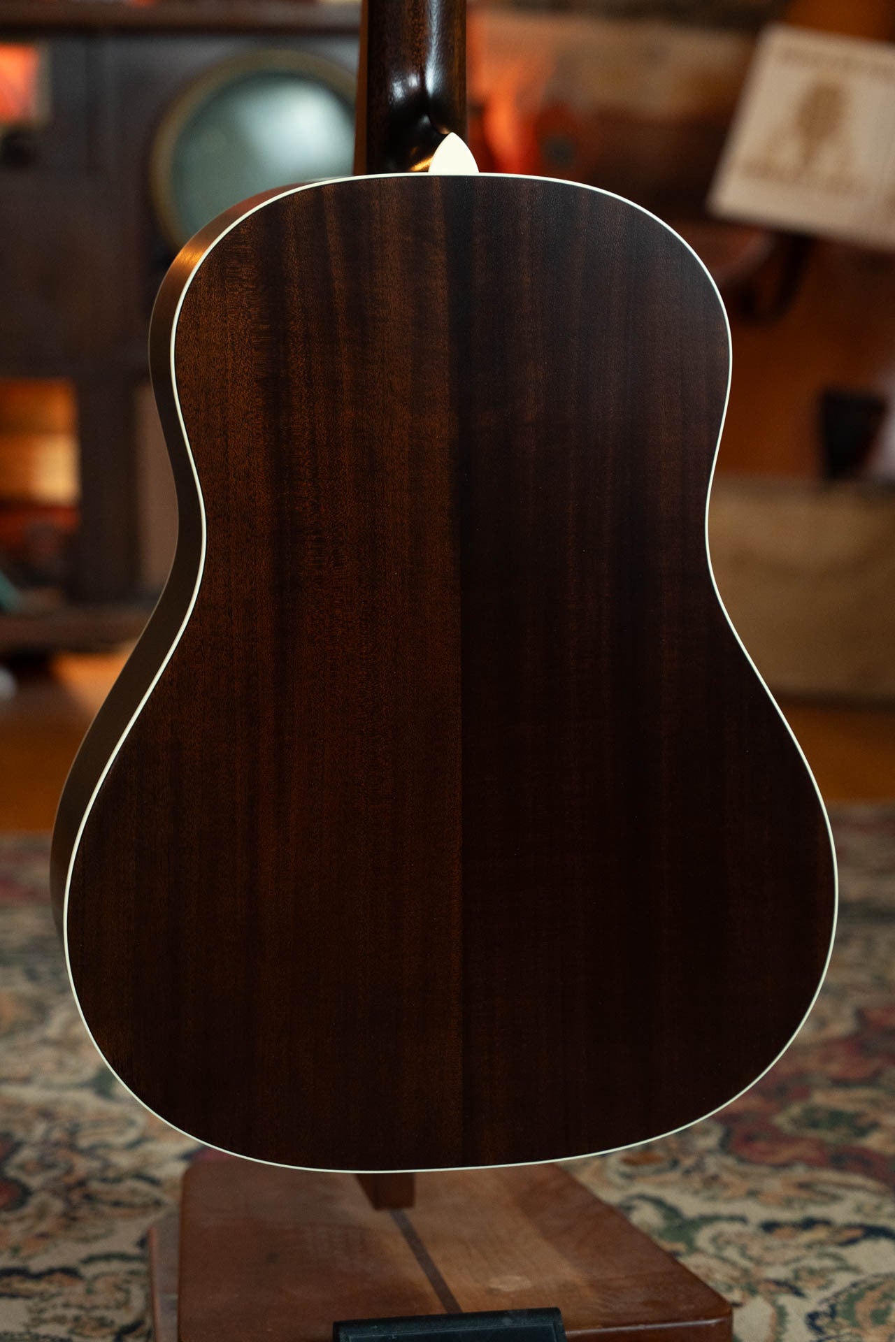 The Boucher Guitars Bourgeois PSN-SD-S Satin Professional Series The Natural Sitka/Mahogany Slope Shoulder Dreadnought Acoustic Guitar #1174 stands upright on a stand, showing its dark wood back with white binding against a patterned rug.
