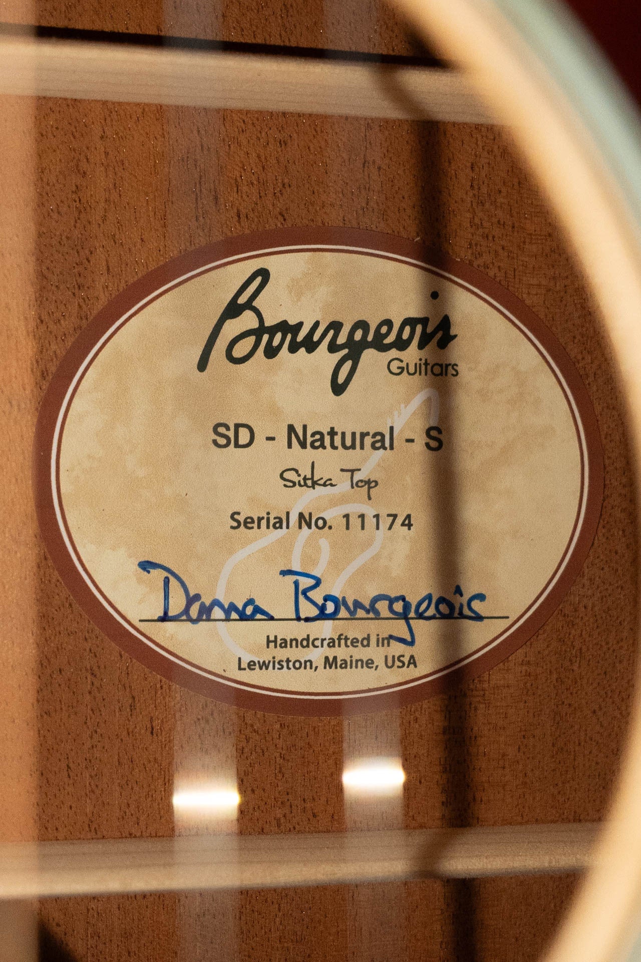 A close-up of a Boucher Guitars PSN-SD-S Satin Professional Series The Natural Sitka/Mahogany Slope Shoulder Dreadnought Acoustic Guitar #1174 label, handcrafted and hand-signed, visible inside the body.