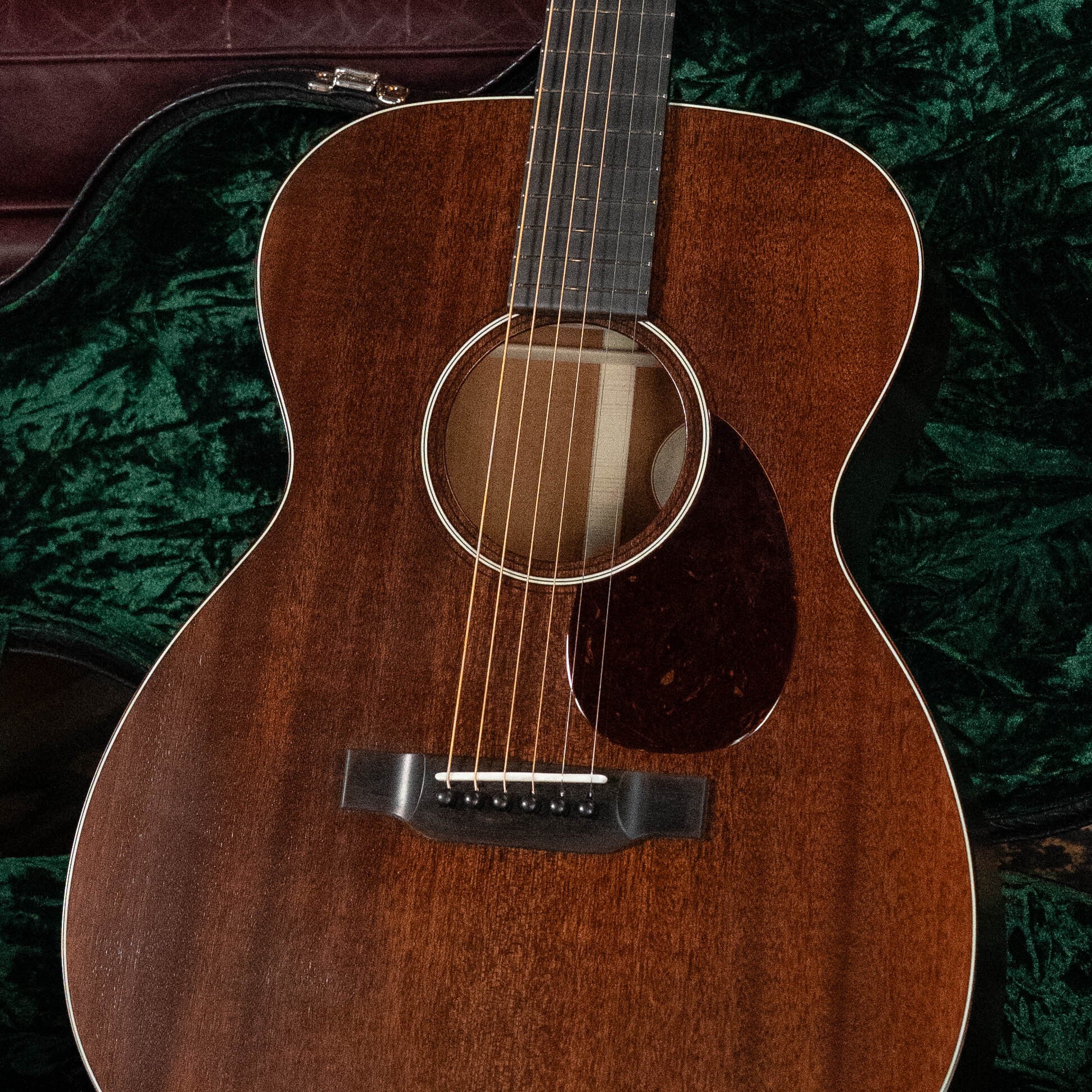 A close-up of the Bourgeois Professional Series Hog Top All Mahogany OM Acoustic Guitar #1208, featuring a rich brown mahogany body, resting inside its green velvet-lined hard case.