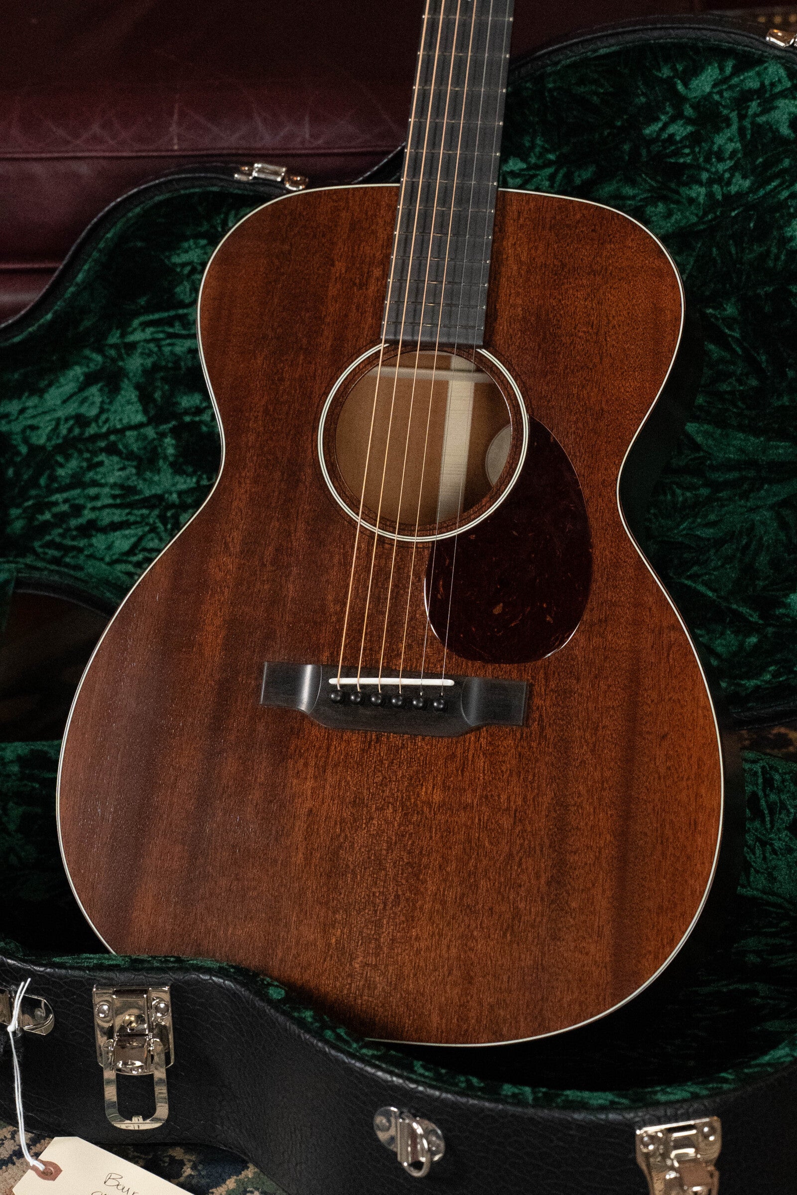 The Bourgeois Professional Series Hog Top All Mahogany OM Acoustic Guitar #1208 features a dark mahogany finish, six strings, small pickguard, and comes in an open black hard case lined with green velvet.