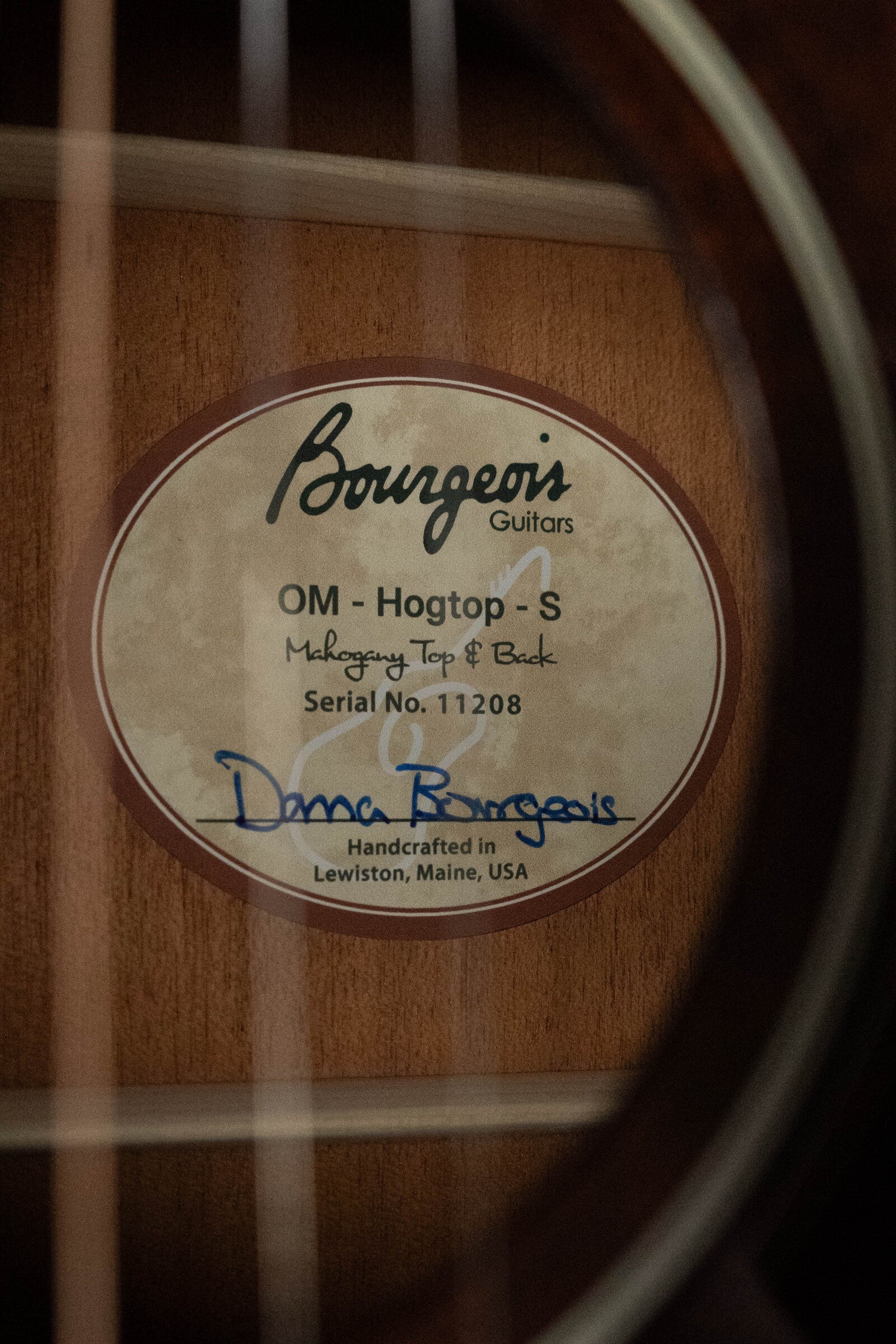 Close-up of the Bourgeois Professional Series Hog Top All Mahogany OM Acoustic Guitar #1208 label, strings in foreground—a premium choice for fingerstyle acoustic players.