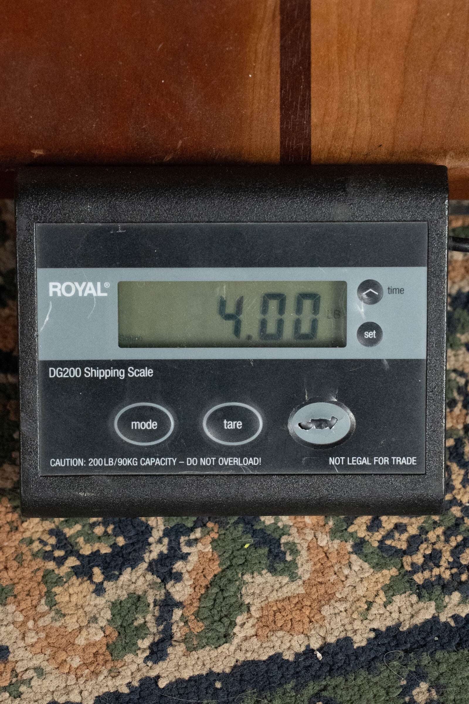 A digital shipping scale shows 4.00 pounds on a patterned carpet, with a Bourgeois Professional Series Hog Top All Mahogany OM Acoustic Guitar (#1208) positioned behind it; buttons and the ROYAL brand are visible on the scale’s front.