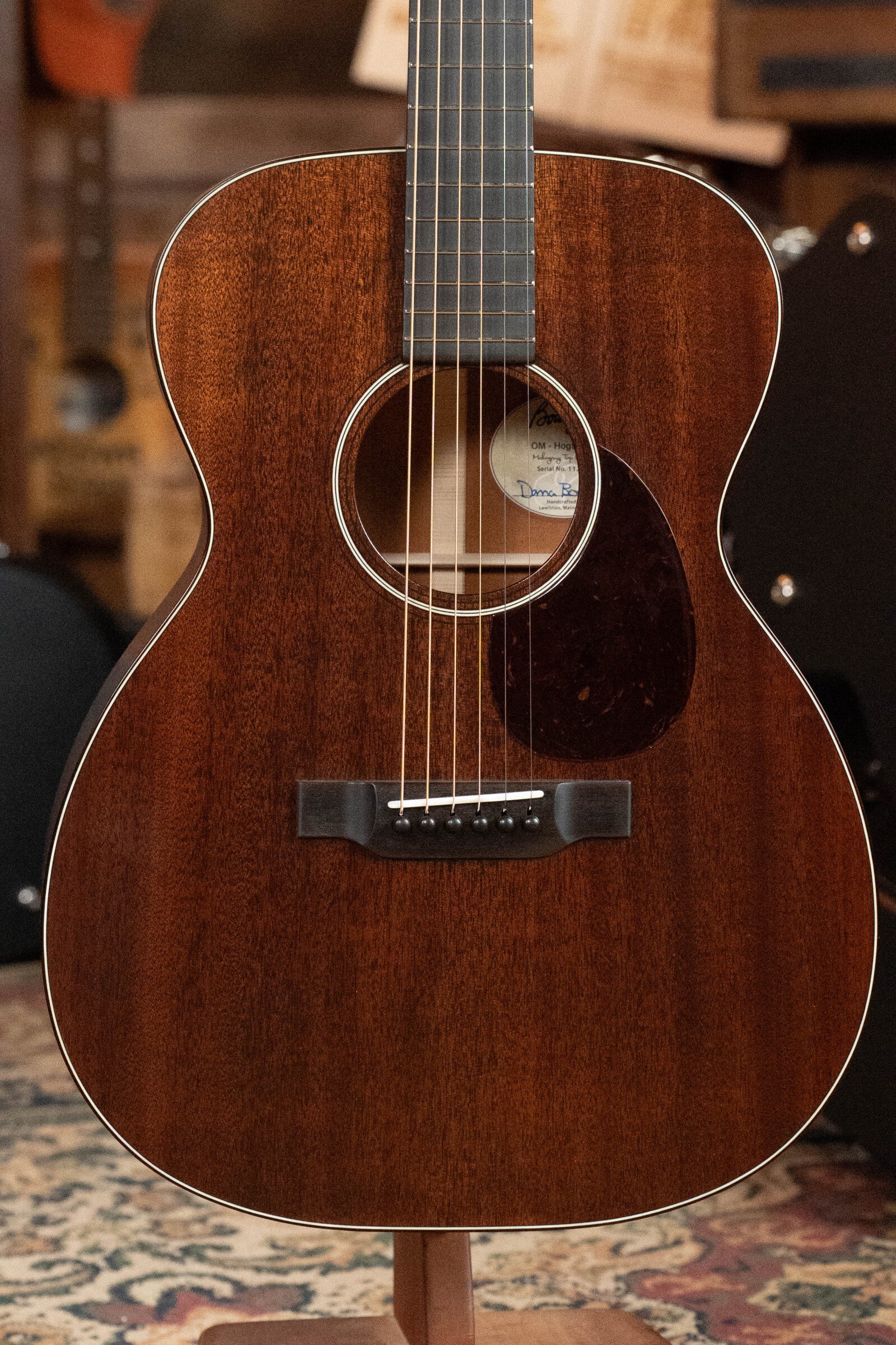 A close-up of the Bourgeois Professional Series Hog Top All Mahogany OM Acoustic Guitar #1208, featuring a dark mahogany finish, round soundhole with white rosette, and tortoiseshell-style pickguard, displayed upright indoors.