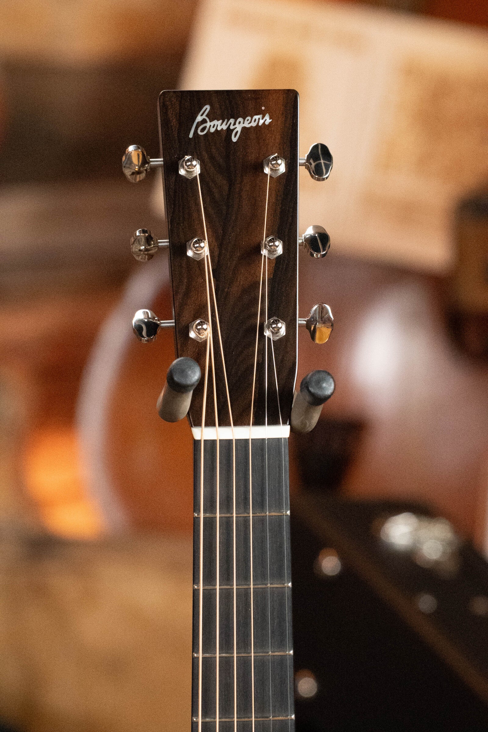 Close-up of the headstock of a Bourgeois Professional Series Hog Top All Mahogany OM Acoustic Guitar #1208, featuring six tuning pegs and part of the fretboard against a softly blurred, warm-toned background.