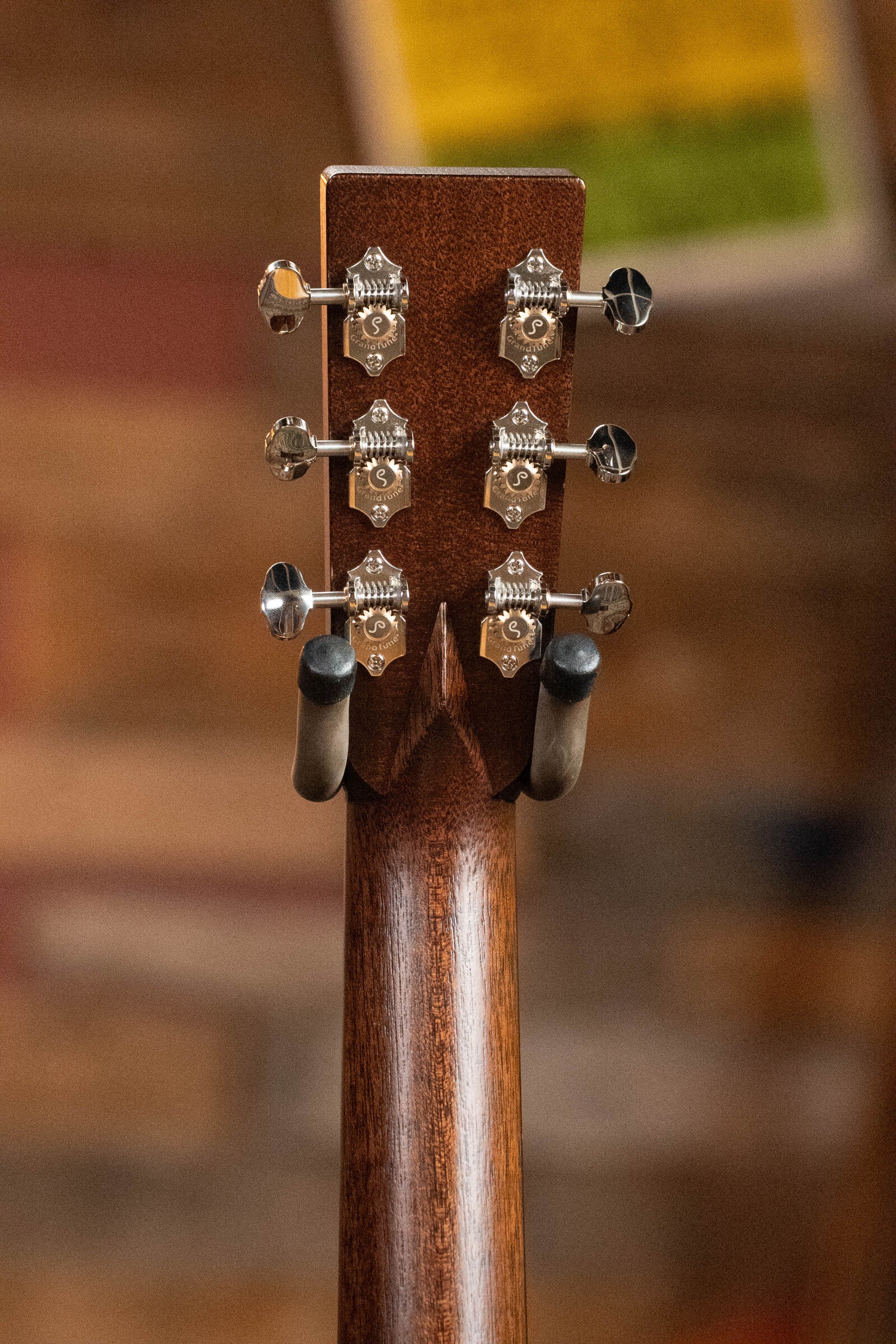 Close-up of the Bourgeois Professional Series Hog Top All Mahogany OM Acoustic Guitar #1208 headstock, displaying six tuning pegs and metal hardware as the guitar rests in a hanger against a blurred wooden background.