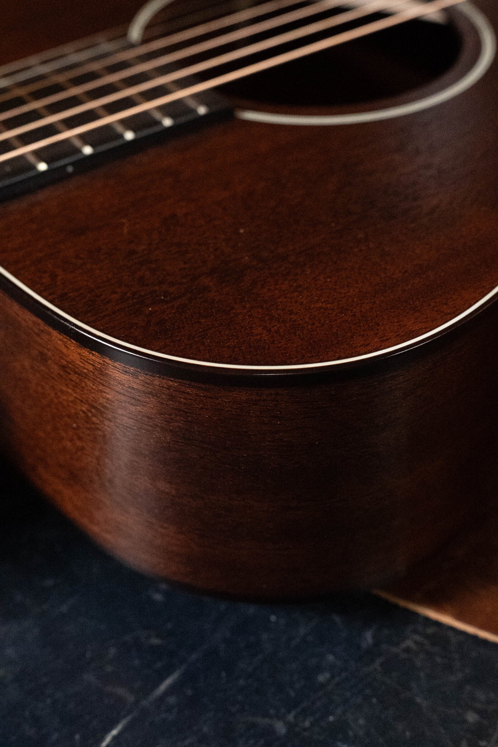 Close-up of the Bourgeois Professional Series Hog Top All Mahogany OM Acoustic Guitar #1208, highlighting its glossy mahogany wood grain, strings, and part of the sound hole against a dark background.