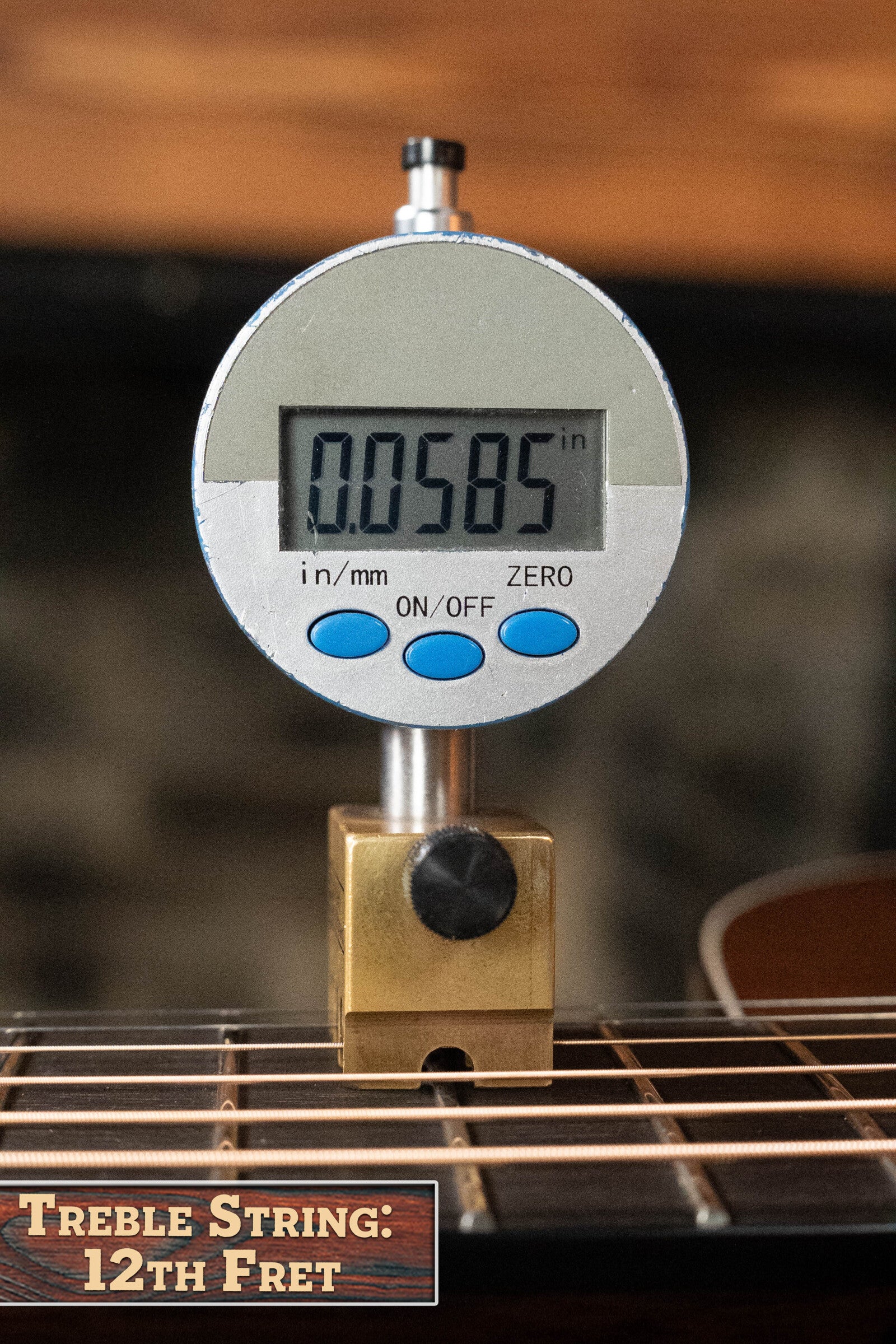 A digital gauge measures 0.0585" at the 12th fret of a Bourgeois Professional Series Hog Top All Mahogany OM Acoustic Guitar #1208. The caption reads: Treble String: 12th Fret. Gauge rests on strings, sitting on a stand. Brand: Bourgeois.