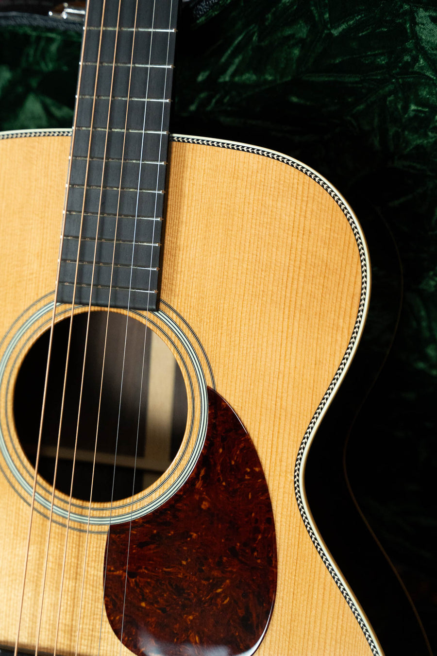 Close-up of the Bourgeois Heirloom Series T-Bar Banjo Tuner Vintage HSV-OM Aged Tone Adirondack/Brazilian Rosewood Orchestra Model Acoustic Guitar #1098, set against a dark green textured fabric background.