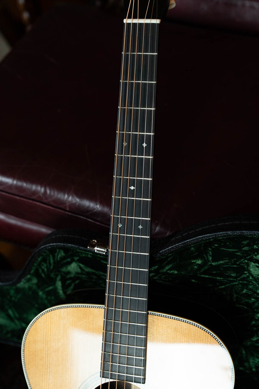 A close-up of the Bourgeois Heirloom Series T-Bar Banjo Tuner Vintage HSV-OM Aged Tone Adirondack/Brazilian Rosewood Orchestra Model Acoustic Guitar #1098, showing its Brazilian rosewood fingerboard and strings in a green-lined case on a leather seat.
