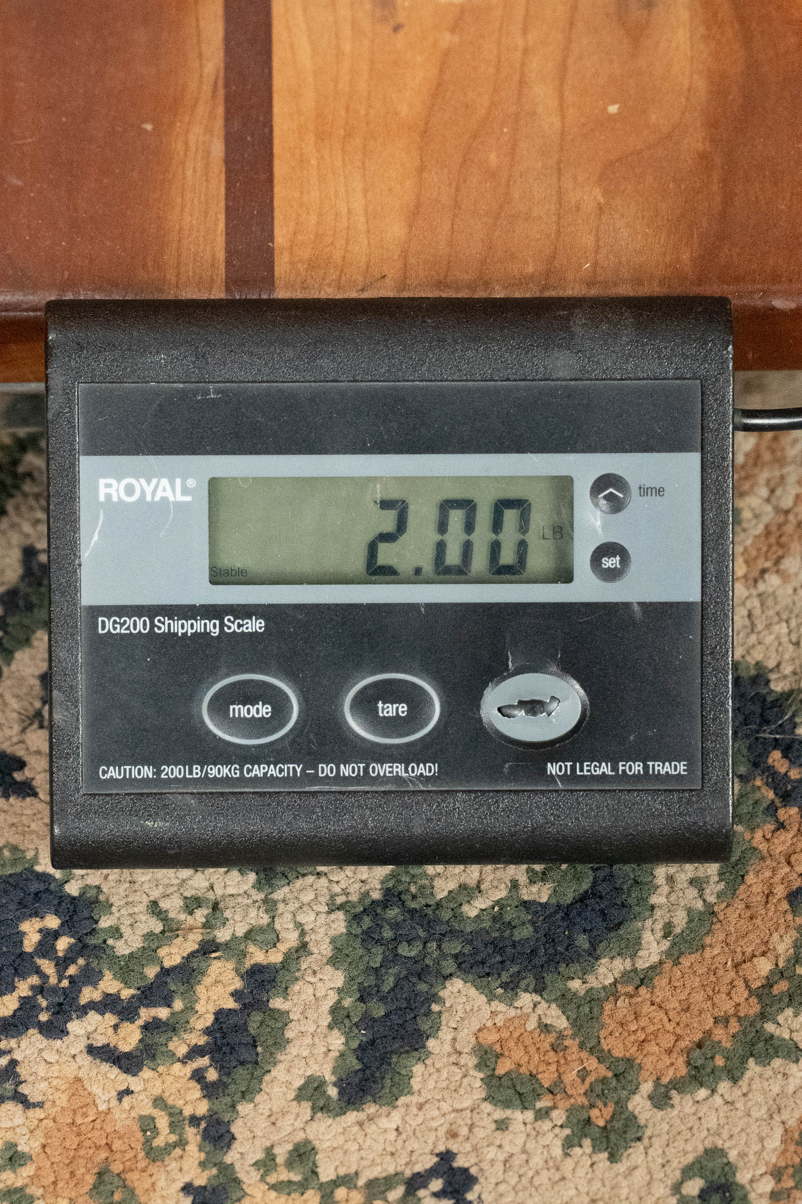 A Bulas Carpathian Spruce/Curly Maple Cremona Sunburst A-Style Mandolin #8129 rests on wood above, while a digital shipping scale on patterned carpet displays 2.00 pounds.