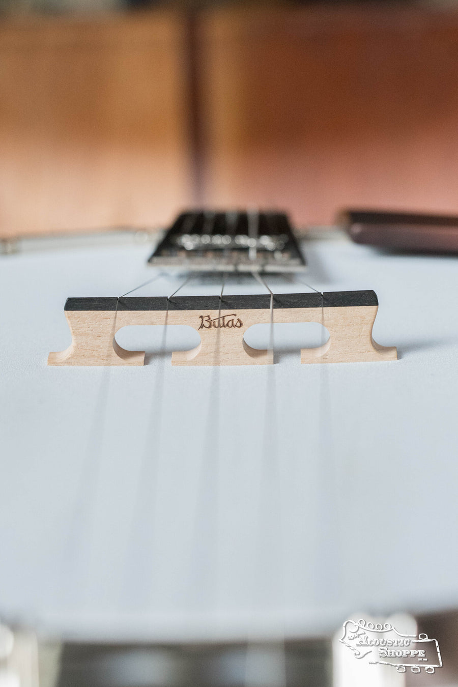 Close-up of the Bulas 5 String Resonator Banjo #0767 bridge engraved with Bulas, highlighting its strings in sharp focus against a warmly blurred background.