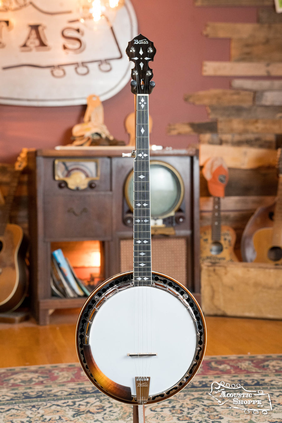 The Bulas 5 String Resonator Banjo #0767, featuring a glossy finish and detailed inlays, stands on display in a rustic room. Its maple rim gleams among wooden walls and vintage decor, highlighting the quality of this Bulas banjo.