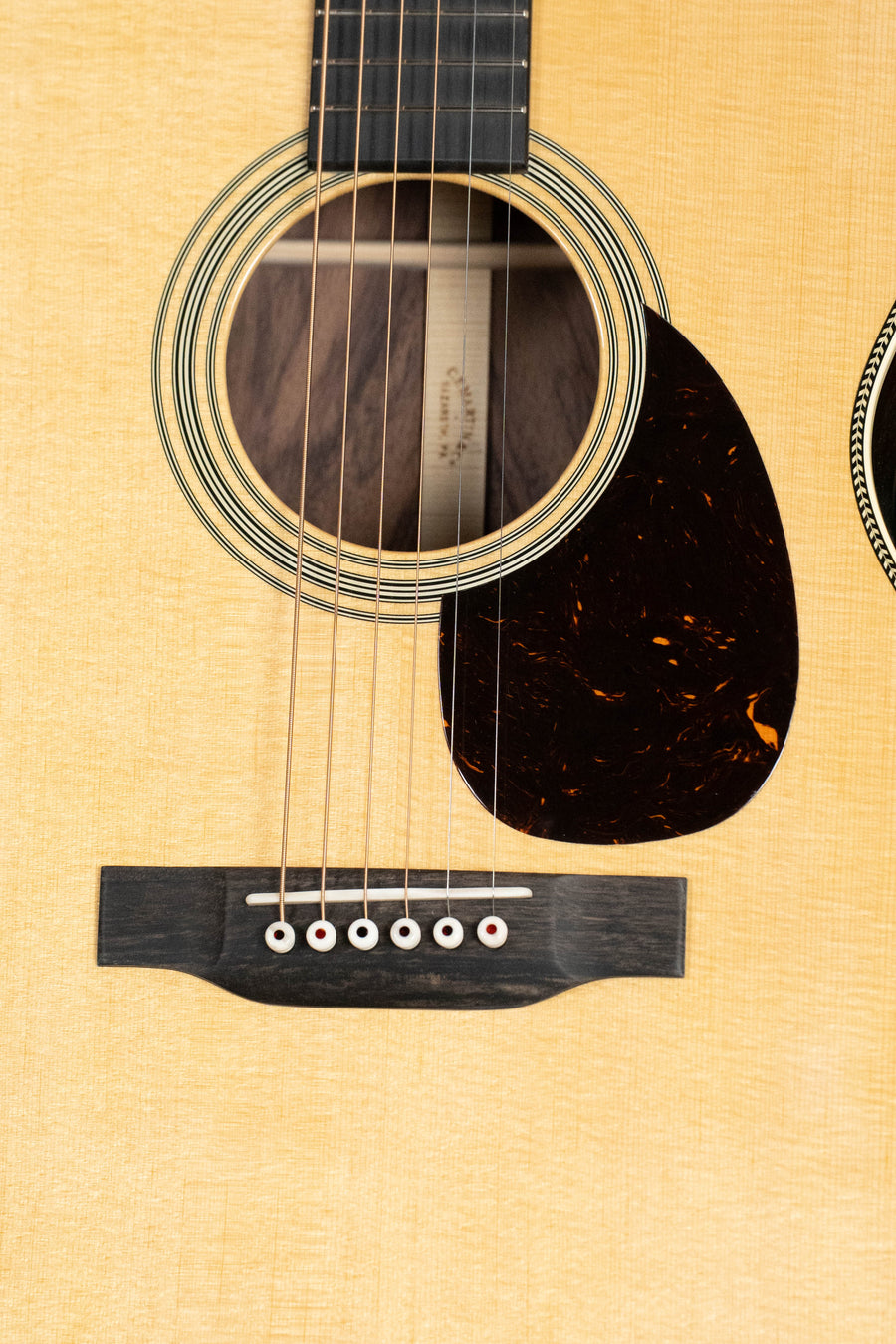 Close-up of a Martin & Co. Custom Shop OOO-28 Style "Wild Grain" East Indian Rosewood Spruce/Indian Rosewood Auditorium Acoustic Guitar, showing its sound hole, strings, bridge, tortoiseshell pickguard, and highlighted wood grain.