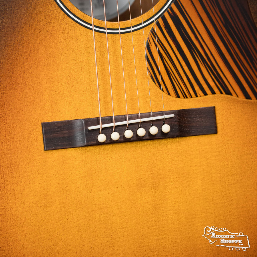 Close-up of an Iris Guitars IRIS DF *Custom* Guild Sitka/Old Mahogany Burst Slope Shoulder Dreadnought Guitar #1044 body, showing the bridge, six strings, wood grain, part of the sound hole, and the Acoustic Shoppe logo in the corner.