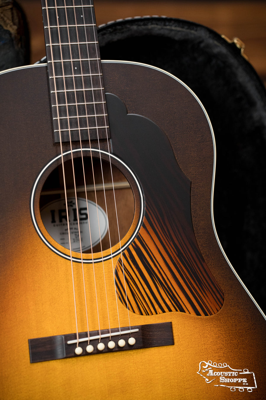 A close-up of the Iris Guitars IRIS DF *Custom* Guild Sitka/Old Mahogany Burst Slope Shoulder Dreadnought Guitar #1044, featuring a sunburst finish and decorative pickguard, resting in an open padded case.