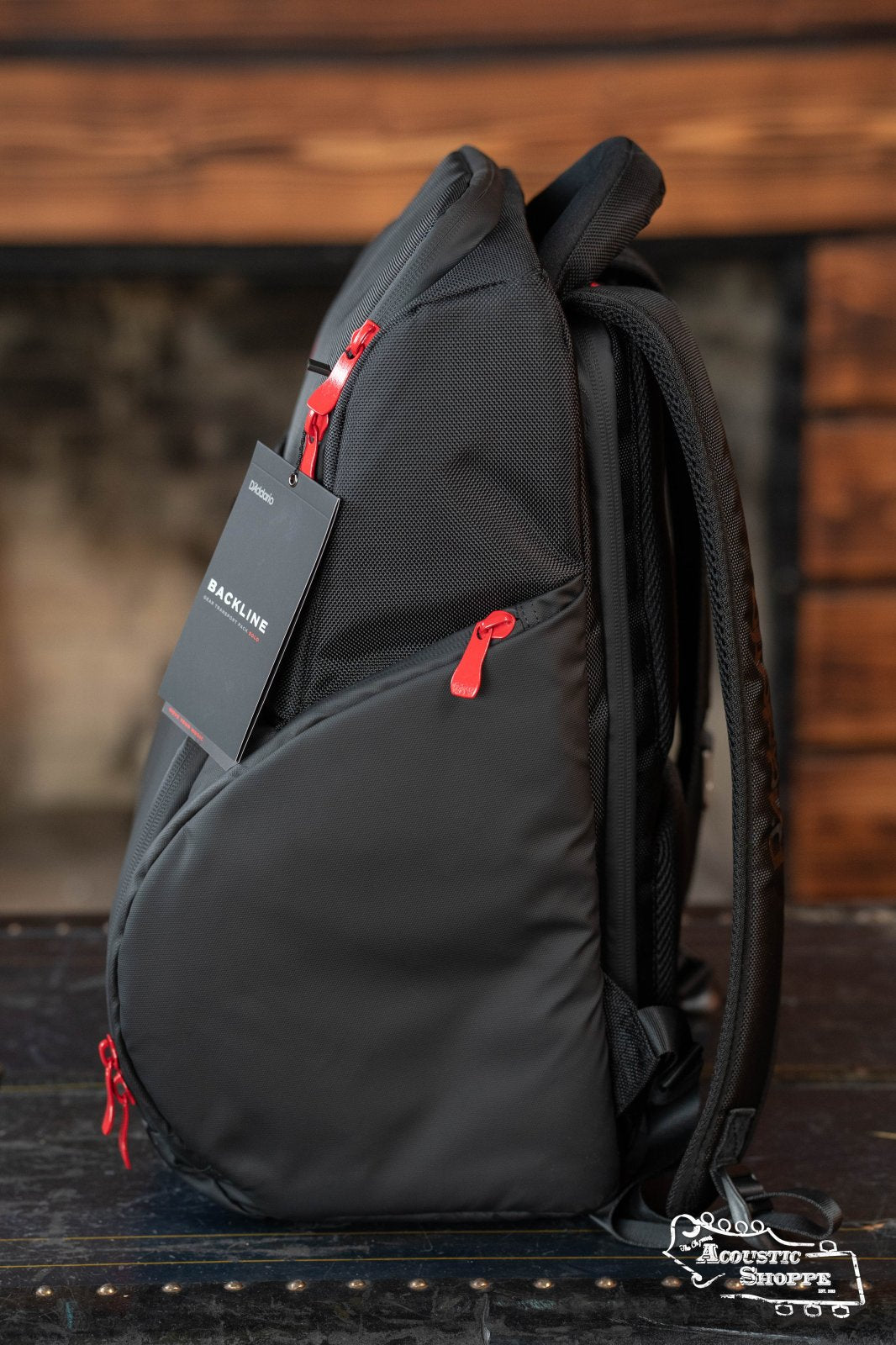 The DAddario Backline Gear Transport Pack Solo, a black musicians backpack with red zippers and BACKLINE tag, rests on a rustic wood table against a blurred backdrop—ideal as your professional gig bag.