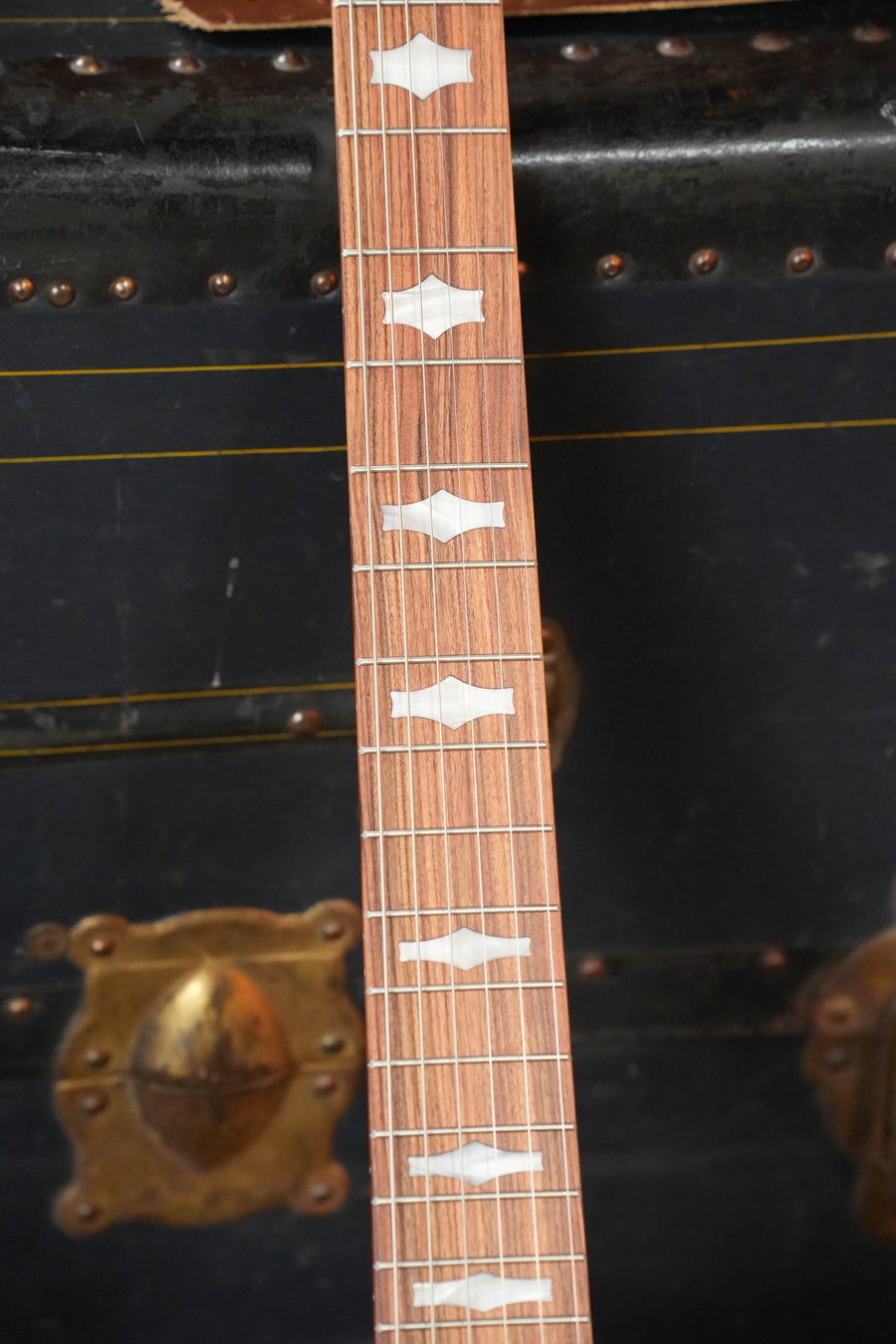 A close-up of the Deering Goodtime 6 R Steel String Banjo w/Kavanjo Pickup by Deering Banjos shows unique white fretboard inlays, set on an old black trunk with brass hardware—ideal for your next acoustic jam.