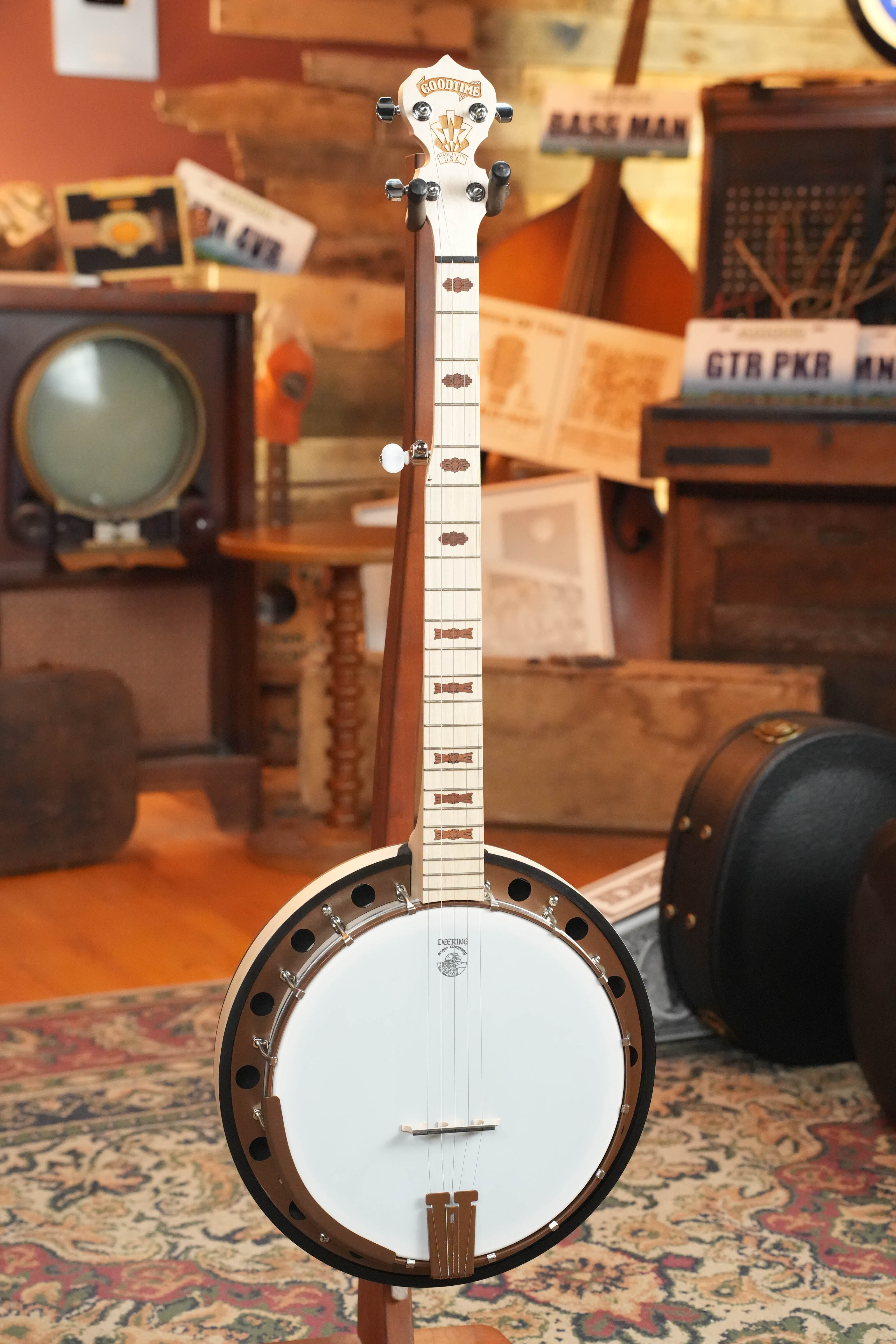 The Deering Goodtime Two 5 String Resonator Banjo #2615 by Deering Banjos stands upright on a patterned rug in a cozy room decorated with vintage musical equipment, wooden accents, and retro furniture.