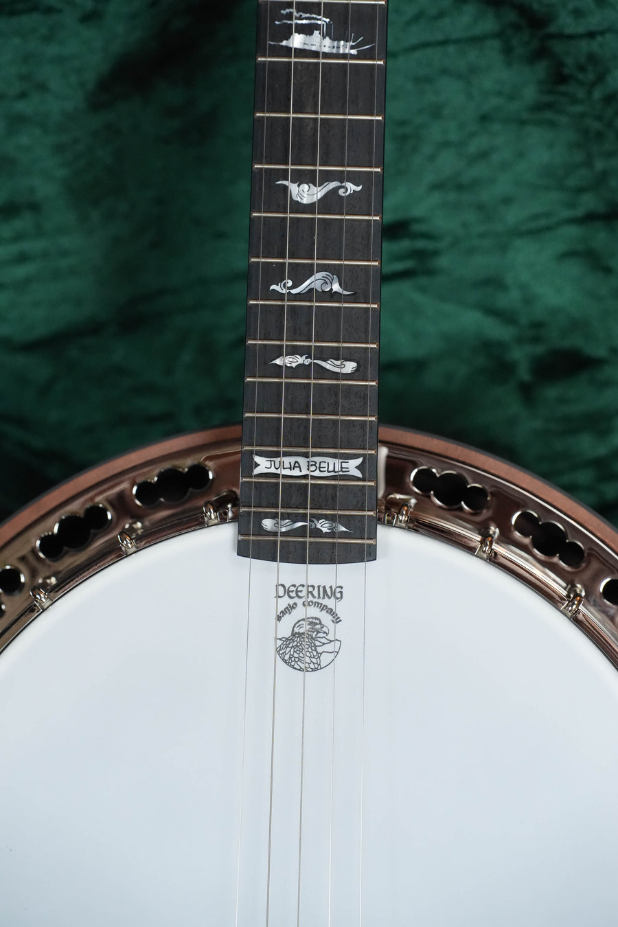 Close-up of a Deering Julia Belle 5 String Resonator Banjo w/Spikes Installed #0067 by Deering Banjos, highlighting intricate fretboard inlays, “Julia Belle” on the neck, and logo on the drumhead—set against green textured background.