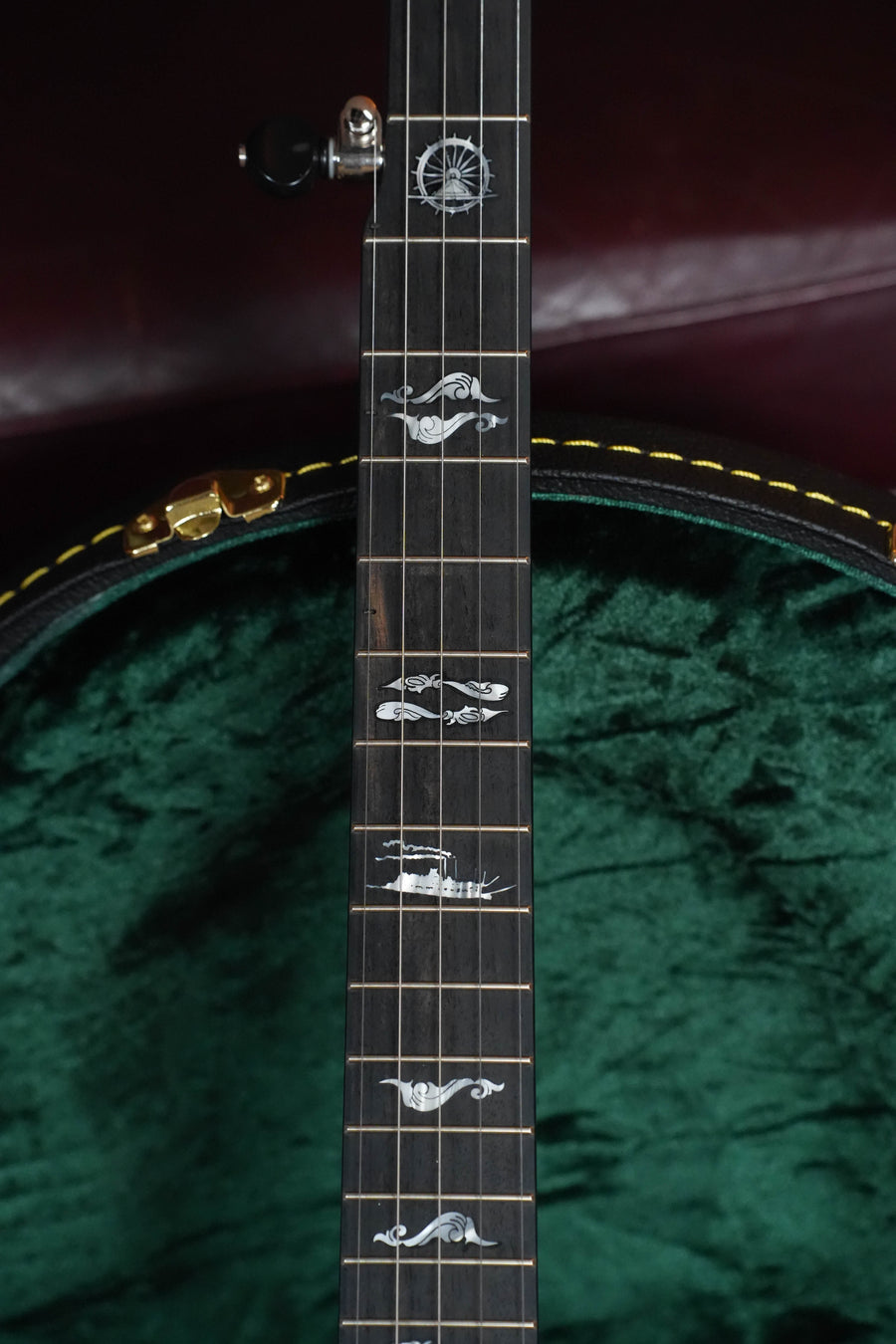 Close-up of the Deering Banjos Julia Belle 5 String Resonator Banjo w/Spikes Installed #0067, showcasing its ornate inlay above a green velvet-lined case—an ideal choice for those seeking a distinctive resonator banjo.