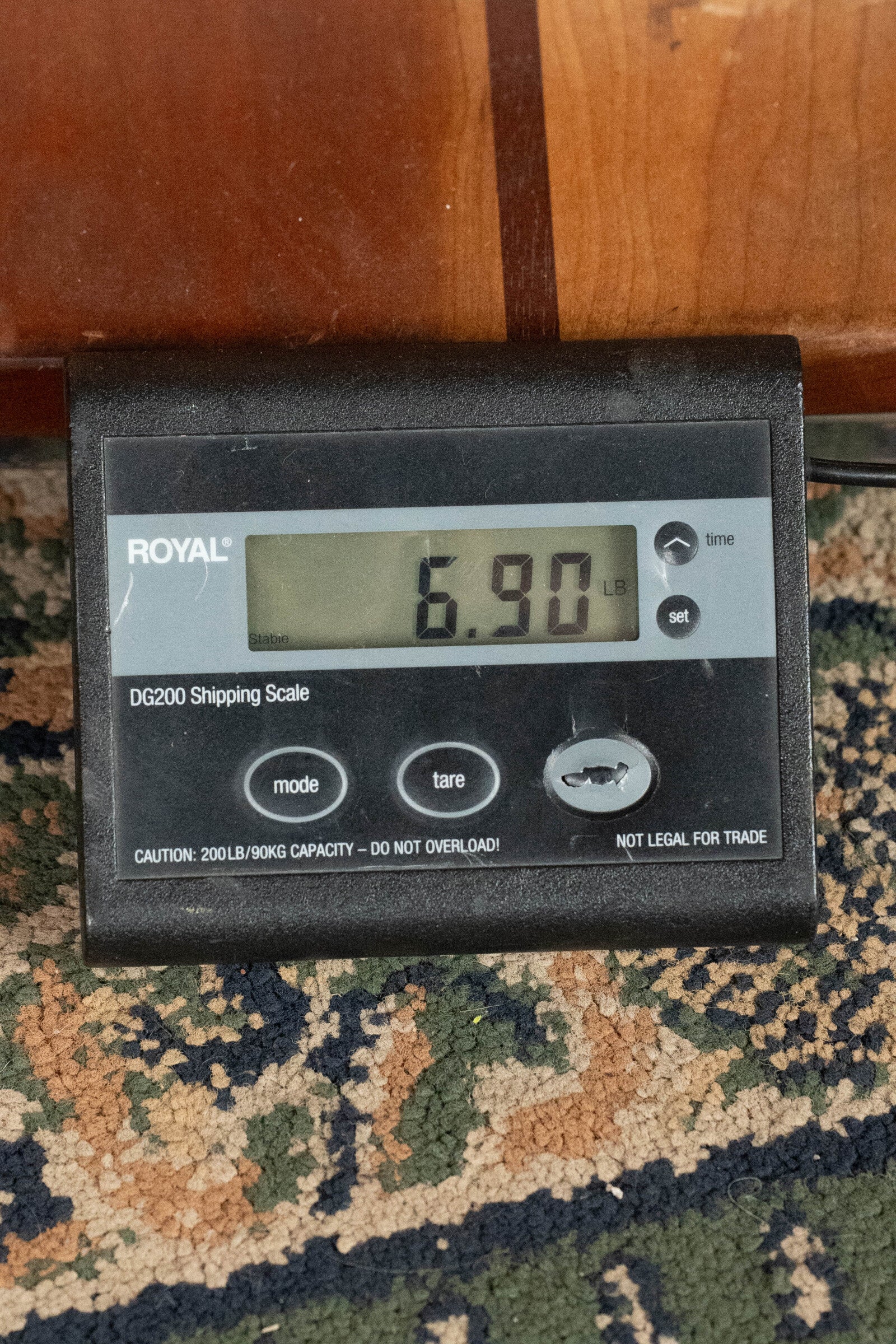 A Deering Goodtime Six-R 6-String Resonator Banjo w/Kavanjo Pickup #2520 from Deering Banjos weighs 6.90 pounds, as shown on a digital shipping scale resting on a patterned carpet.