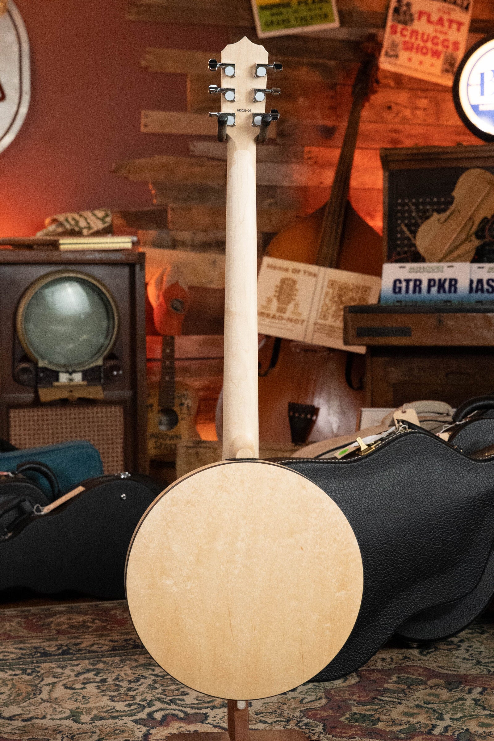 The Deering Goodtime Six-R 6-String Resonator Banjo w/Kavanjo Pickup by Deering Banjos stands upright in a cozy, vintage-style room filled with musical instruments, an old TV, and nostalgic signs and decor in the background.
