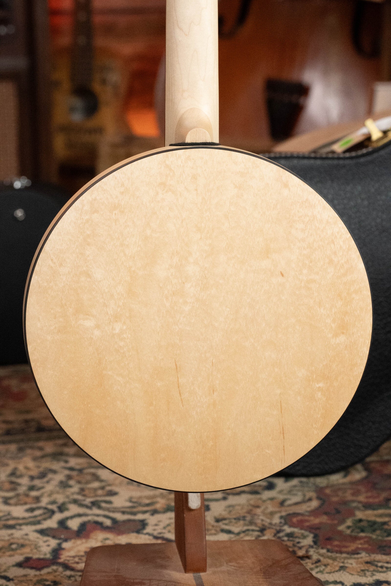 A close-up of the Deering Goodtime Six-R 6-String Resonator Banjo w/Kavanjo Pickup by Deering Banjos rests on a stand, with a blurred background featuring another string instrument and patterned carpet.