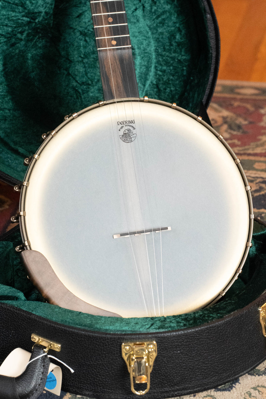 A close-up of a Deering Vega Vintage Star 5-String Openback Banjo w/Spikes #BB66 by Deering Banjos in a green velvet-lined hardshell case, showing its white drum head, metal hardware, open lock, and attached tags.