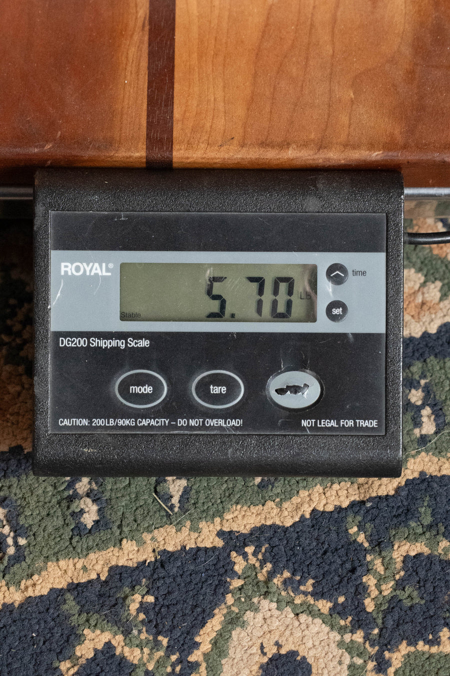 A digital shipping scale labeled ROYAL DG200 shows 5.70 pounds with a Deering Vega Vintage Star 5-String Openback Banjo w/Spikes #BB66 from Deering Banjos resting on top, all set on a patterned carpet.