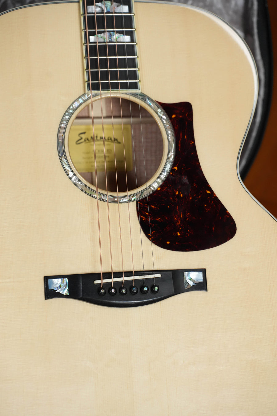 Close-up of a (Used) Eastman AC630-BD Jumbo Acoustic Guitar #7984 by Eastman Guitars, showing its Engelmann spruce top, sound hole, bridge, tortoiseshell pickguard, decorative inlays, and partially visible interior label.
