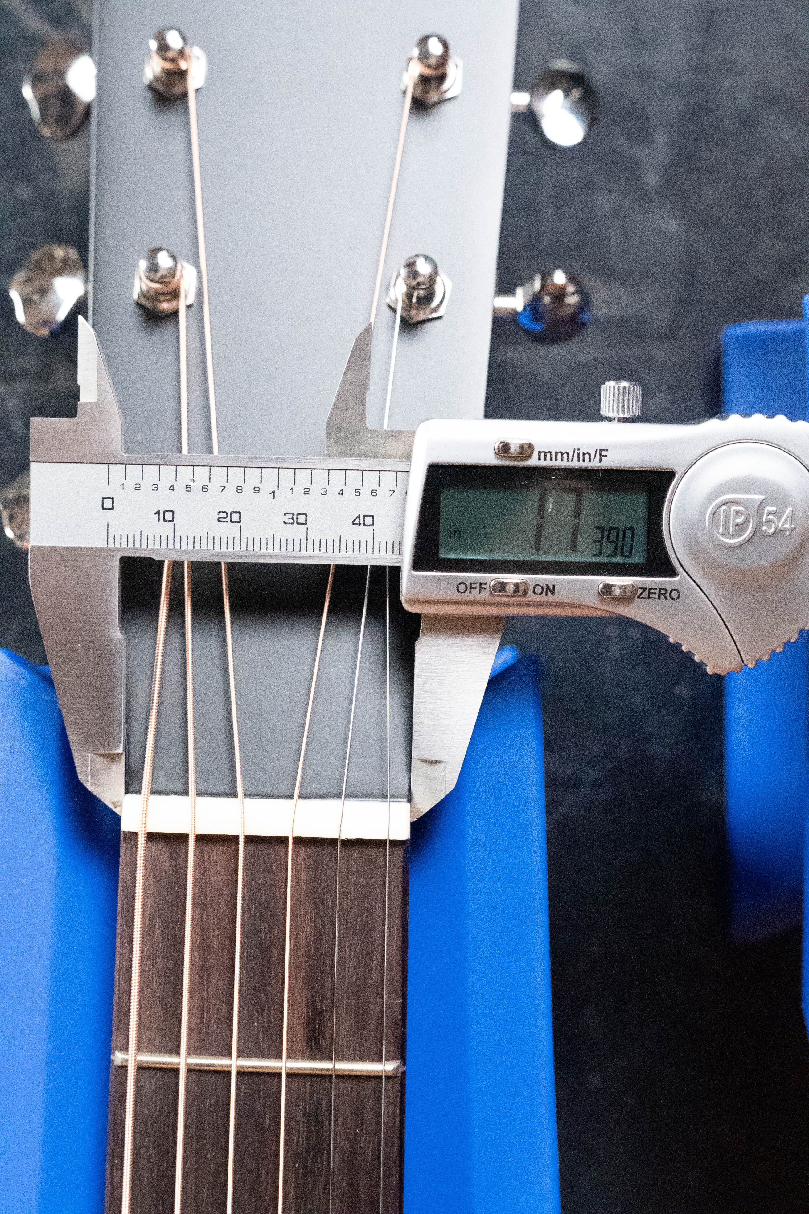A digital caliper measures the Eastman Guitars *Dread-Not Certified Used* E6-LGSS-TC-SB guitar neck at the nut, reading 39.0mm, as its sunburst mahogany body rests on blue holders.