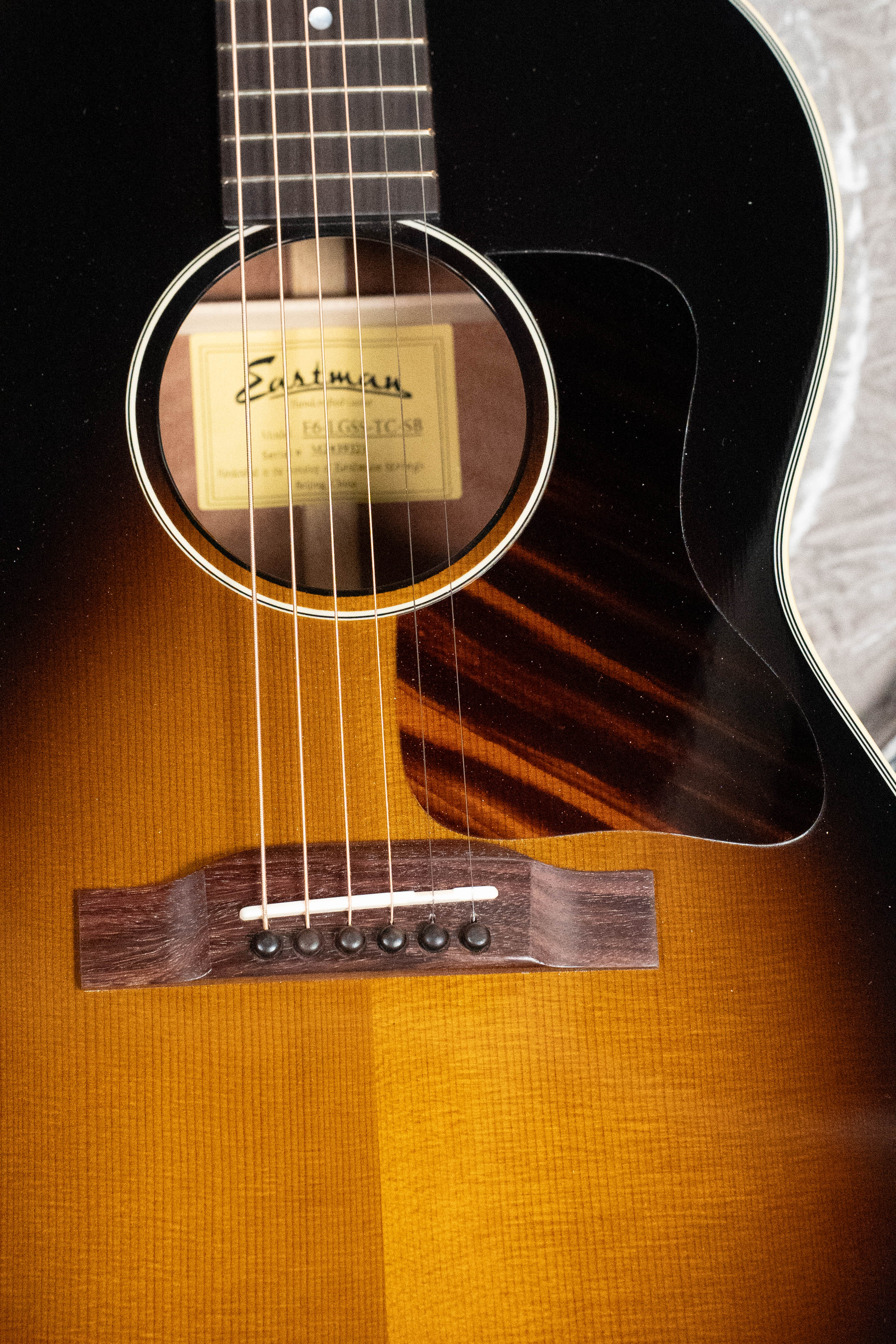 Close-up of a *Dread-Not Certified Used* Eastman Guitars E6-LGSS-TC-SB #9323: features a thermo-cured Sitka spruce top, mahogany body, sunburst finish, strings, sound hole, six-pin bridge, dark brown pickguard, and interior label.