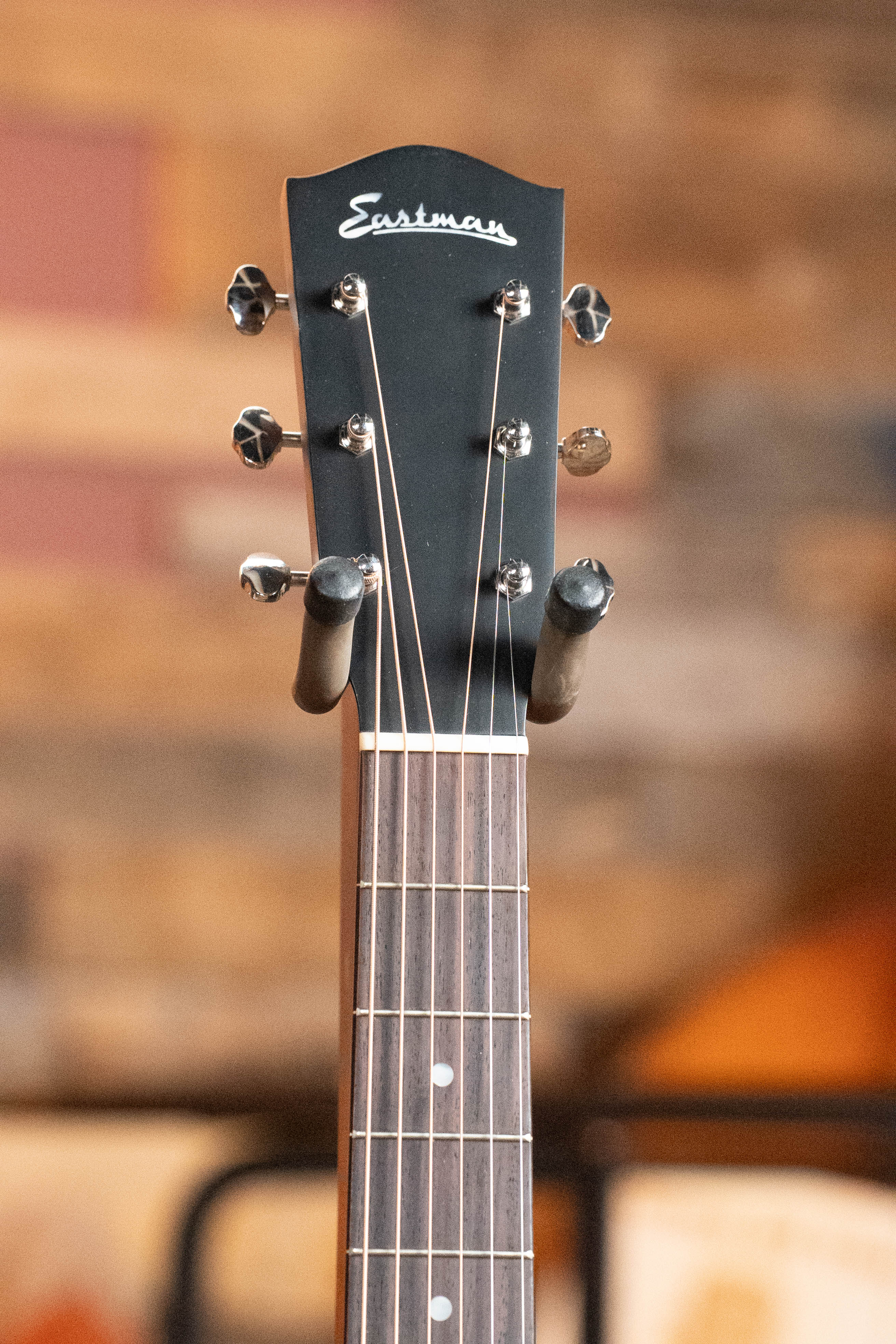 Close-up of the headstock and upper neck of an *Eastman Guitars Dread-Not Certified Used* E6-LGSS-TC-SB Thermo-Cured Sitka/Mahogany Slope Shoulder Sunburst Acoustic Guitar #9323, tuning pegs and strings visible against a warm, blurred background.