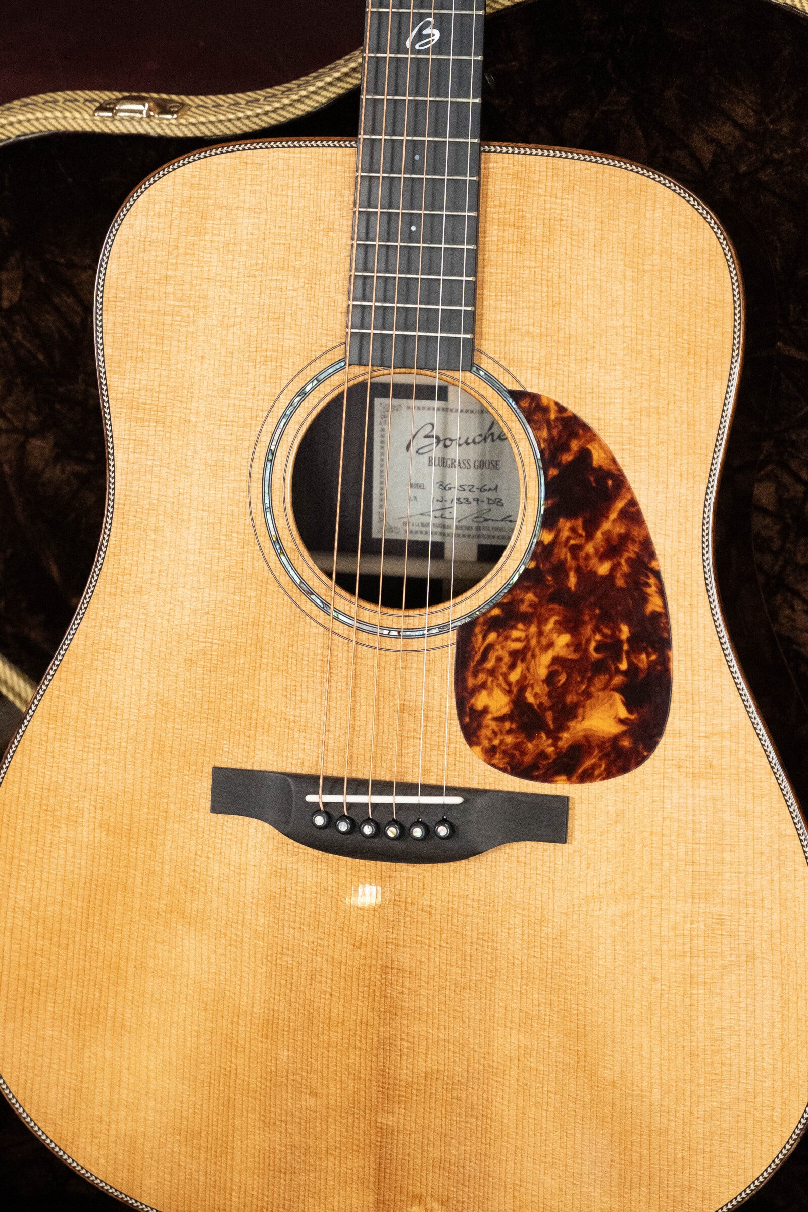 A close-up of the *Dread-Not Certified Used* Boucher BG-52-GM Bluegrass Goose Series Dreadnought by Boucher Guitars, showing its Adirondack Red Spruce top, strings, black tortoiseshell-pattern pickguard, and part of the soundhole label.